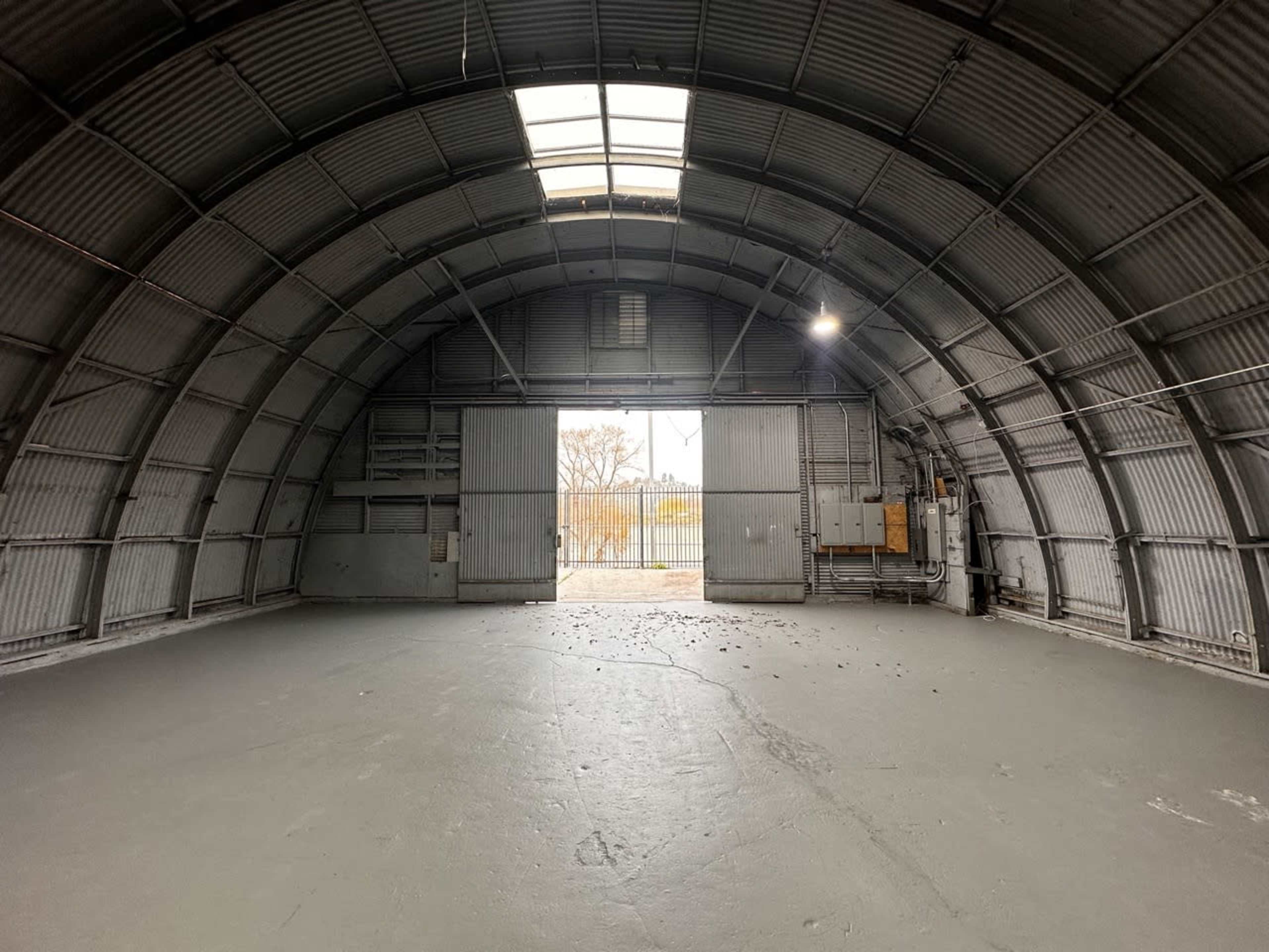 An empty industrial warehouse with a large arched roof and a wide entrance allowing natural light to enter.