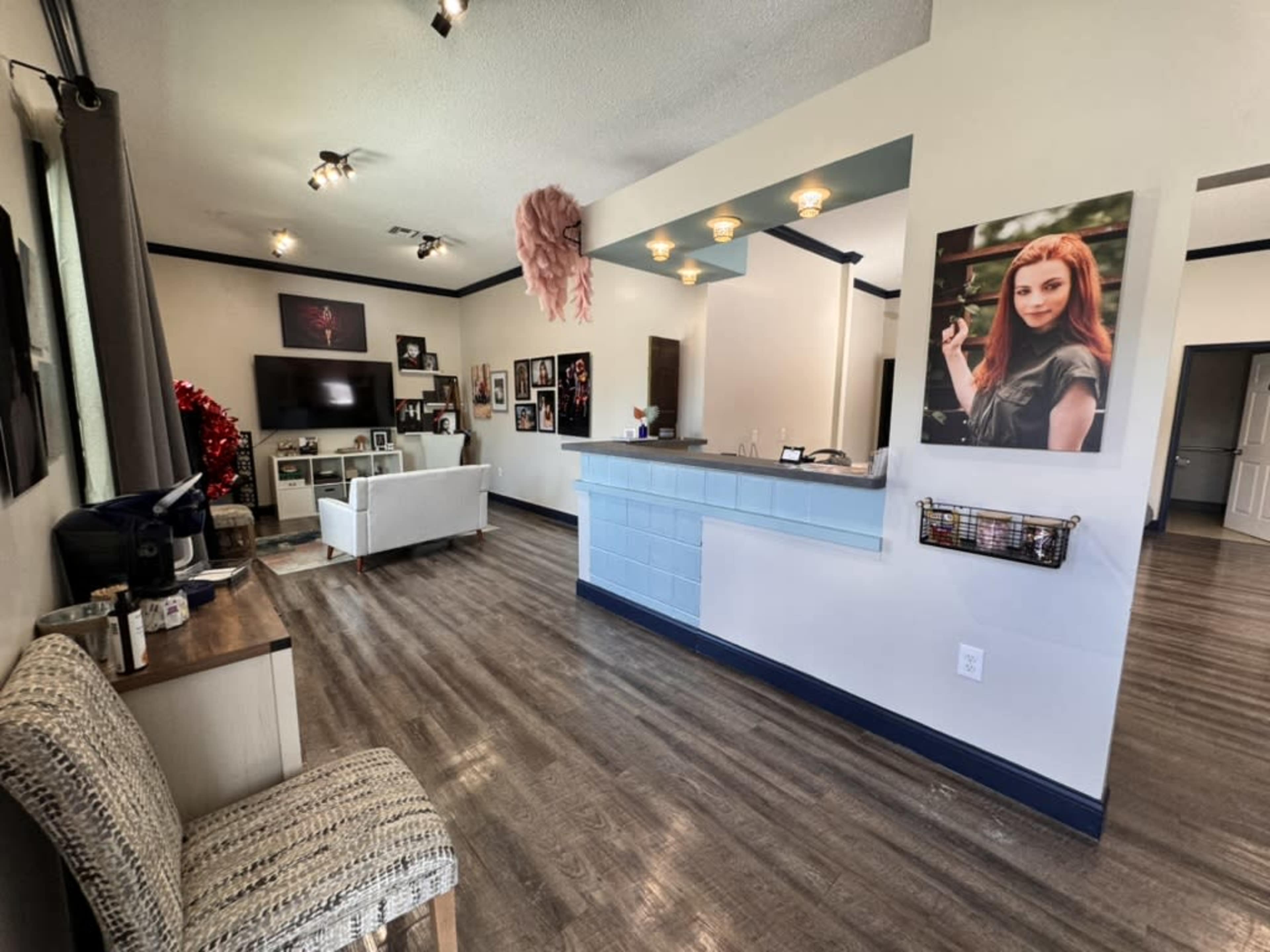 The image shows a spacious room with a reception area, featuring a modern bar counter, seating, and walls adorned with various framed pictures.