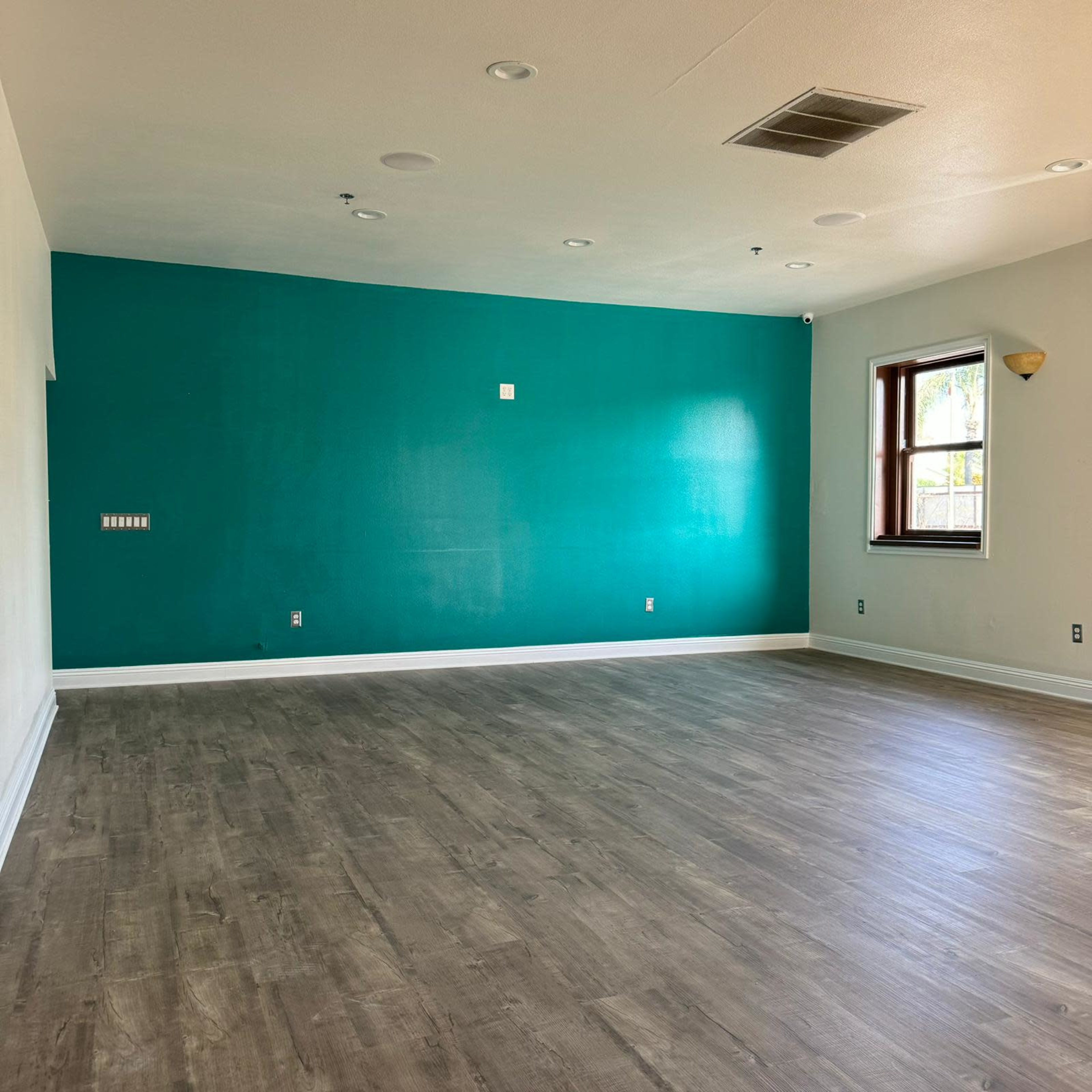 An empty room with a teal accent wall and wooden flooring.