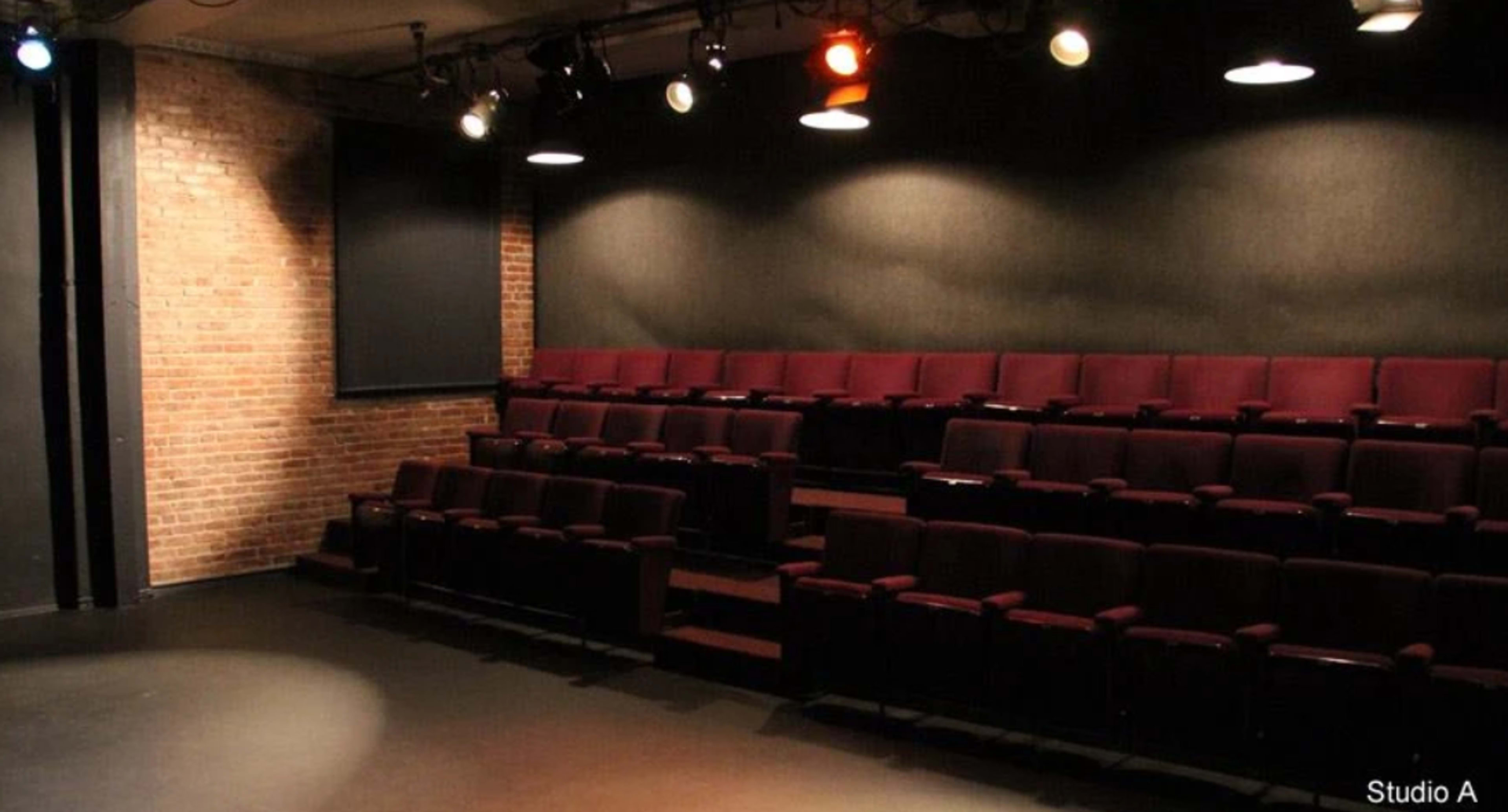 The image shows an empty theater with maroon seating arranged in a semi-circle facing a dark stage.