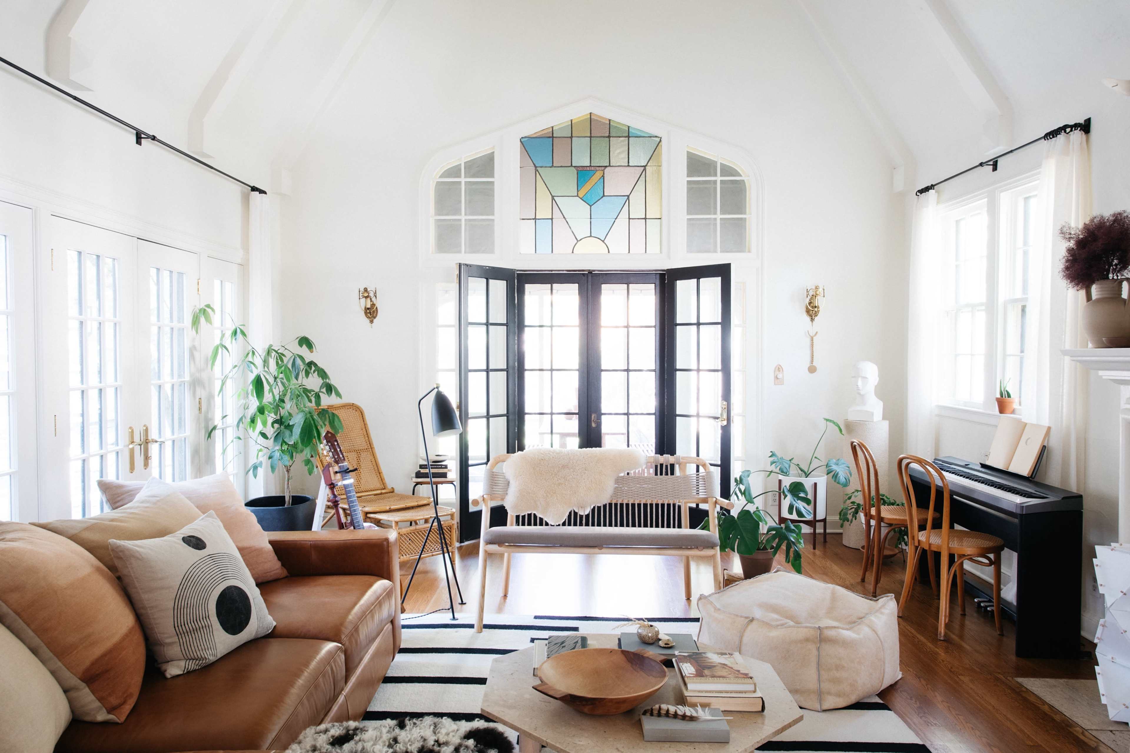 A bright living room with large windows, a mix of comfortable seating, indoor plants, and a stylish decorative stained glass window.