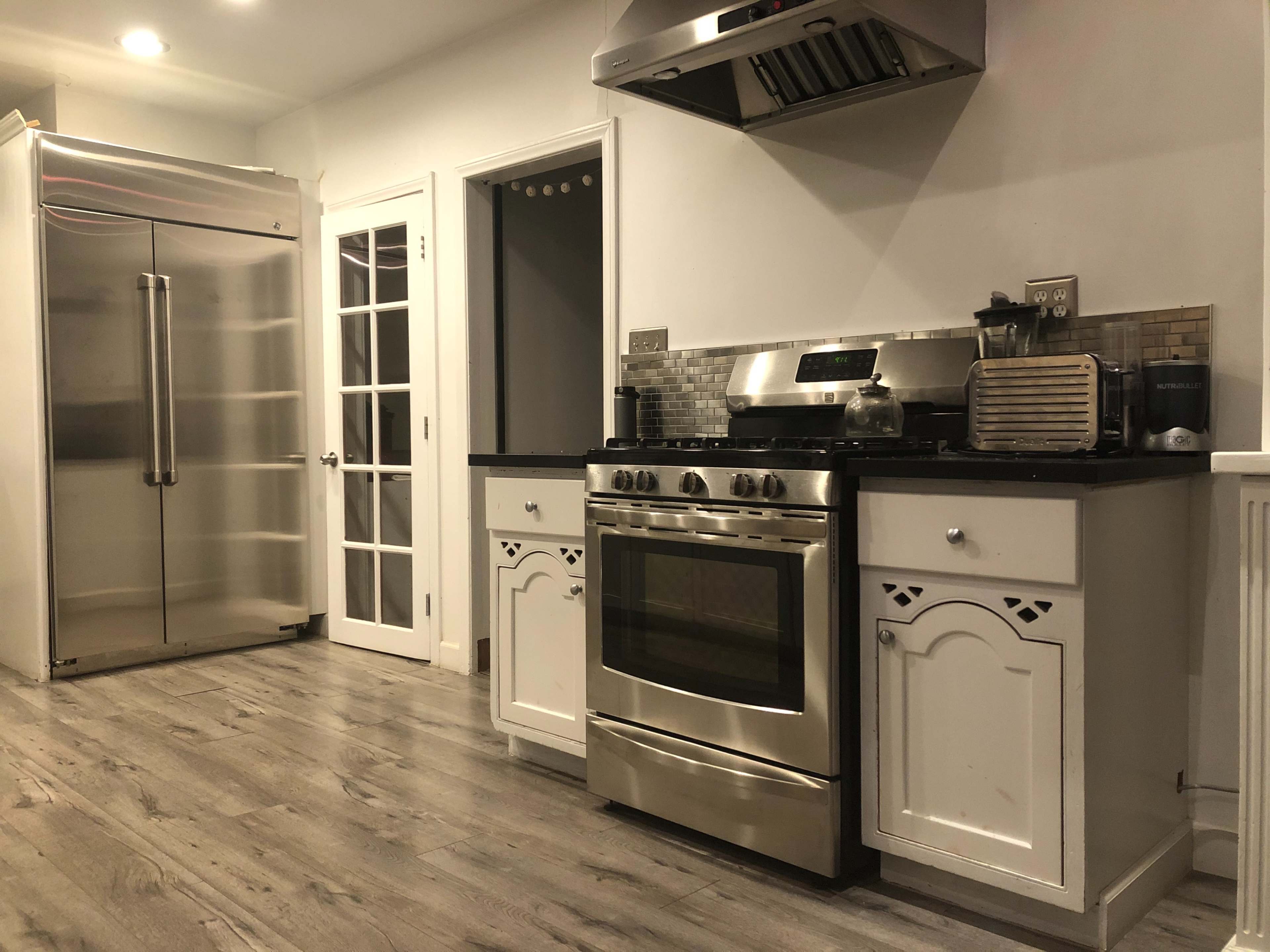 A modern kitchen with stainless steel appliances, including a refrigerator and a stove, set against light-colored cabinetry and a dark countertop.