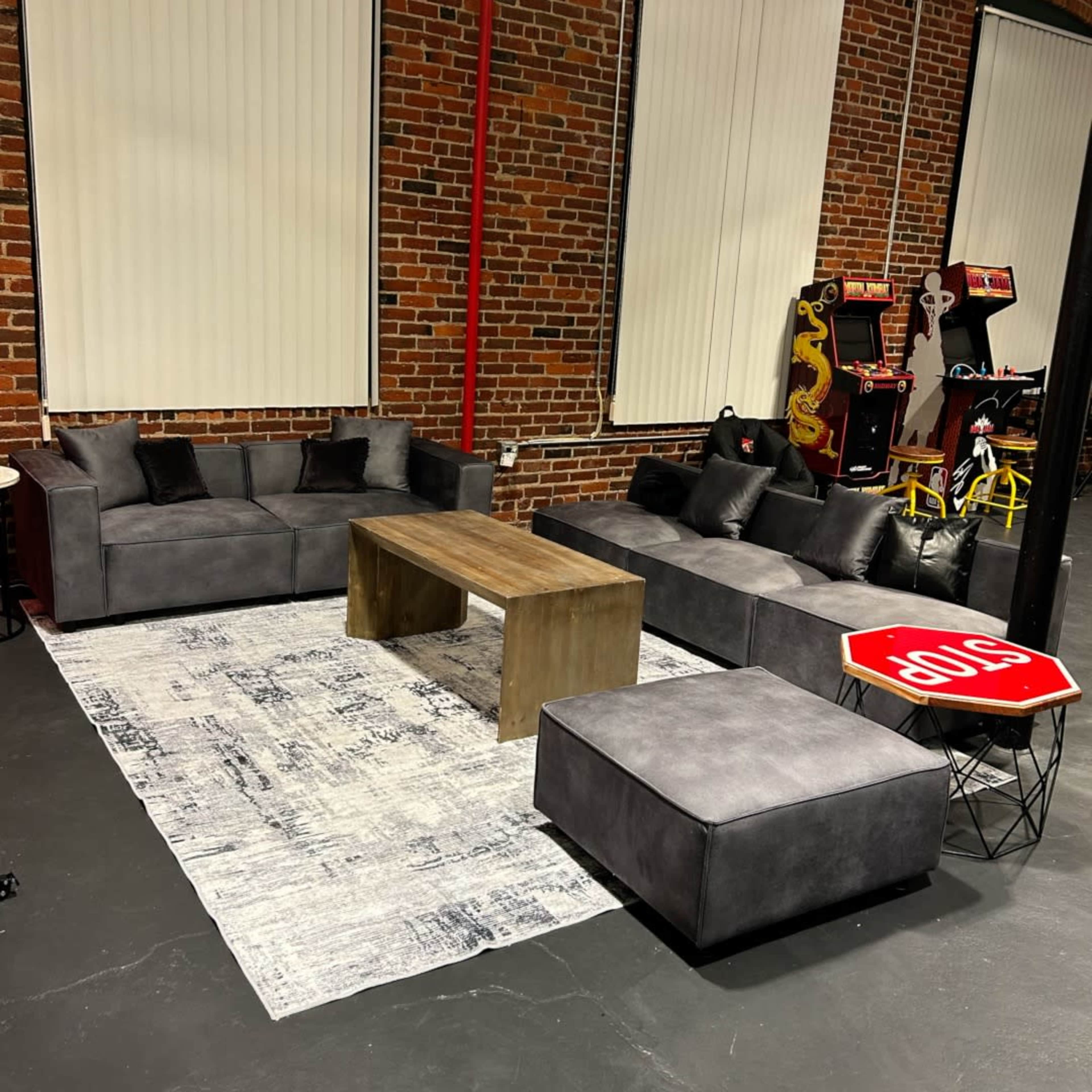A modern seating area with gray sofas, a wooden coffee table, and a stop sign table, set against a brick wall.