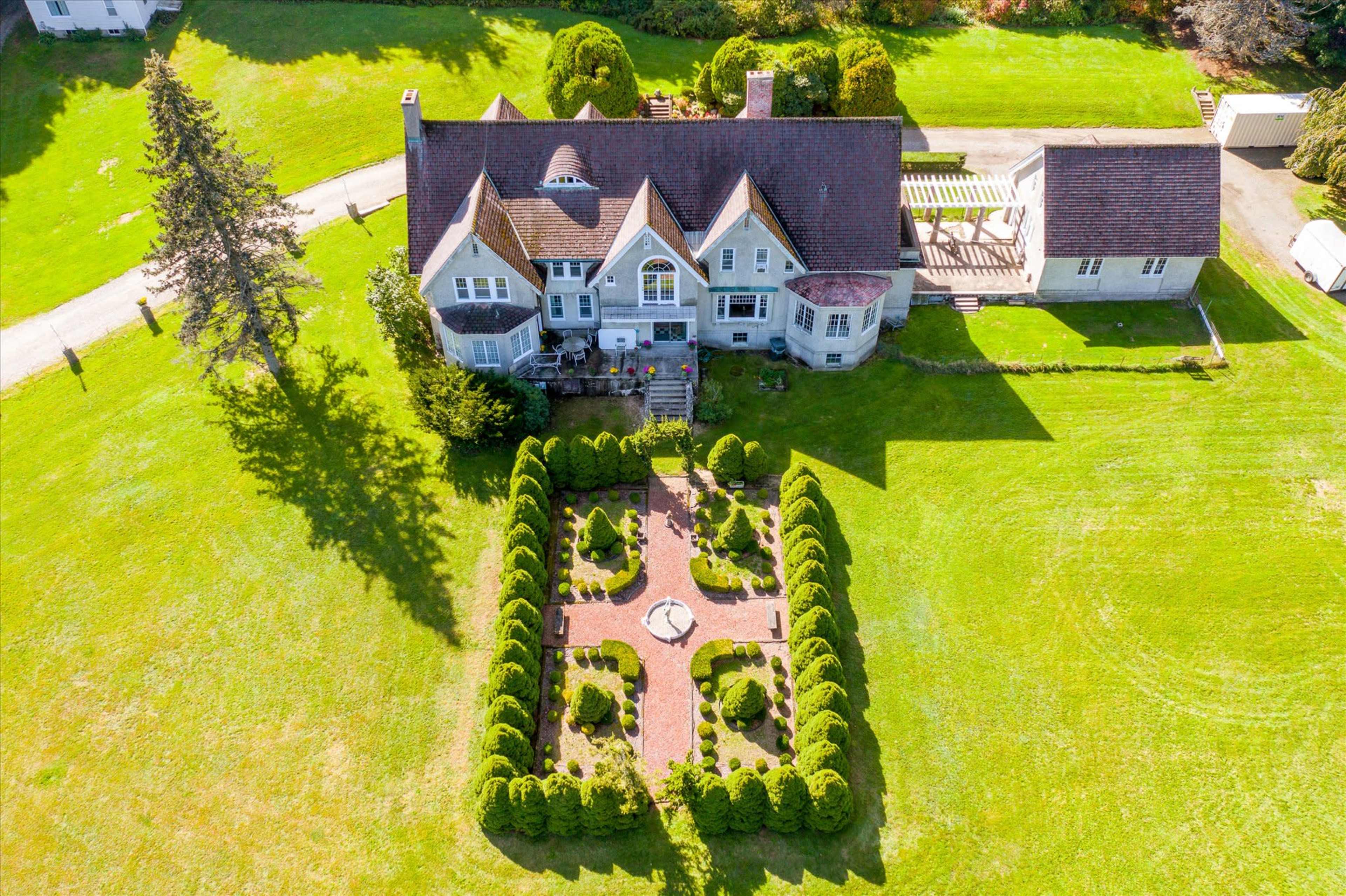 A large, multi-story house surrounded by manicured lawns and a formal garden with hedges and a central pathway.