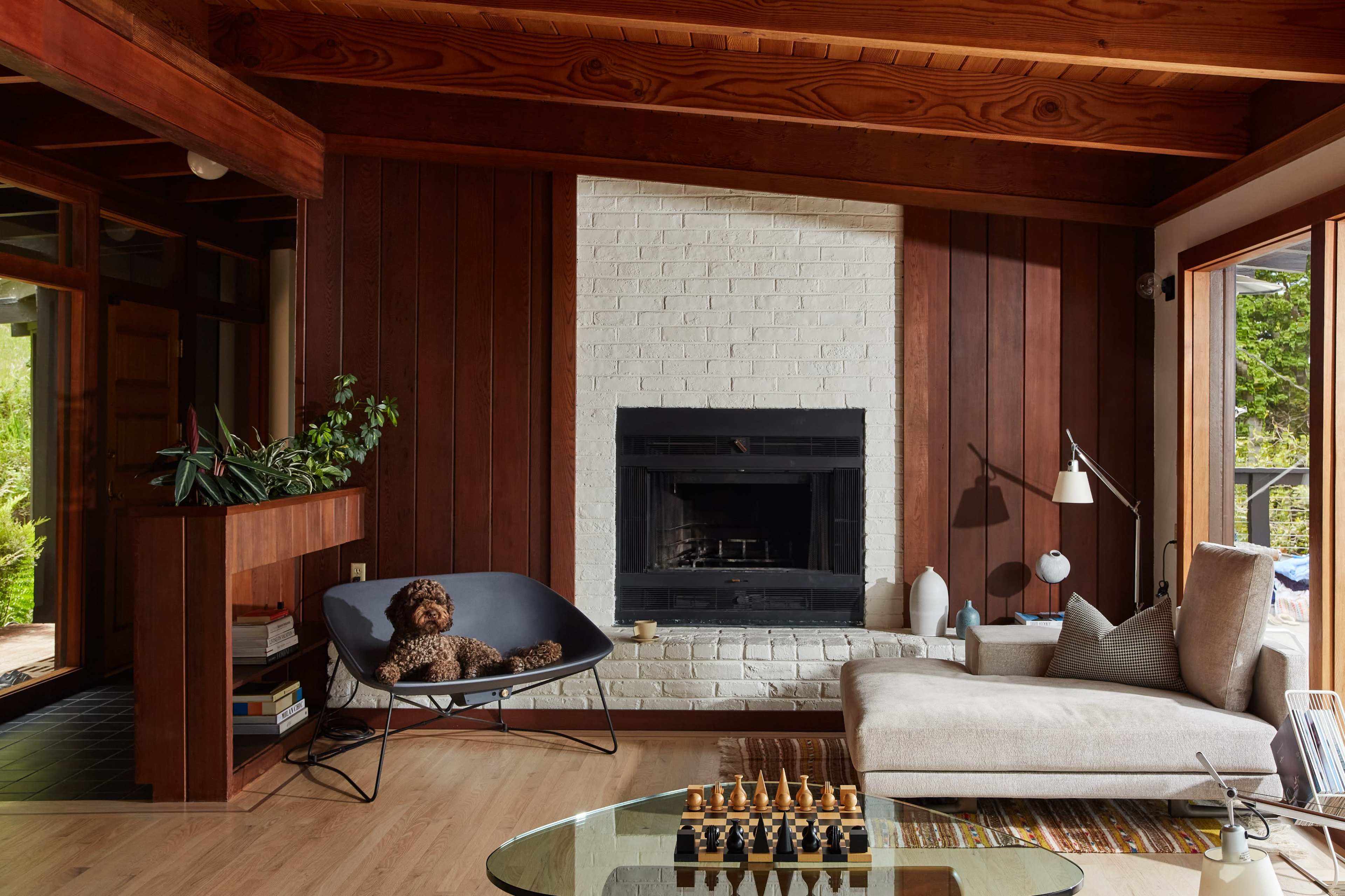 A cozy living room features a large sectional sofa, a modern coffee table, a brick fireplace, and a dog resting on a chair.