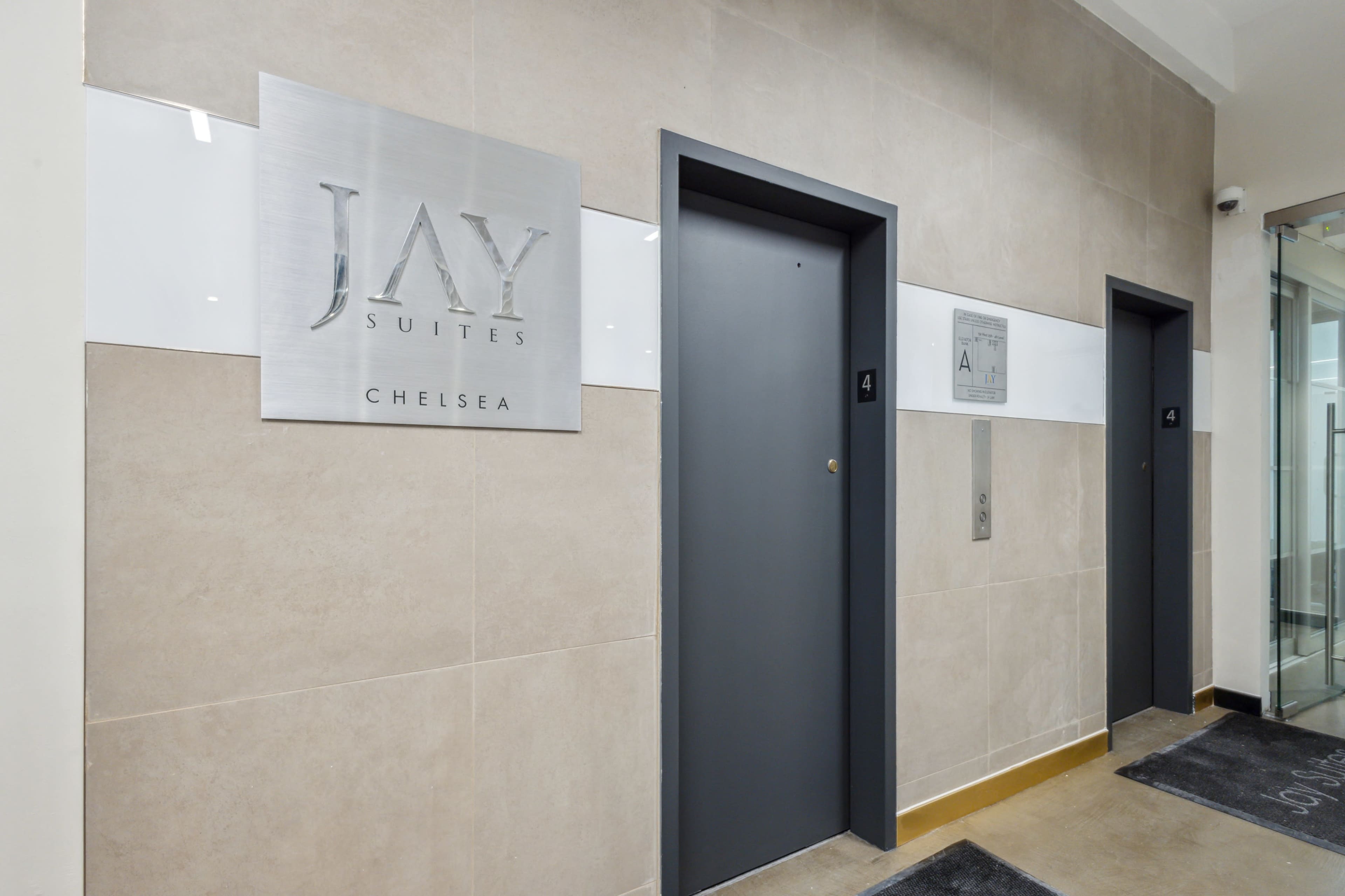 The entrance to a hotel or suite with a sign labeled "JAY SUITES CHELSEA" and two elevator doors, numbered 4.
