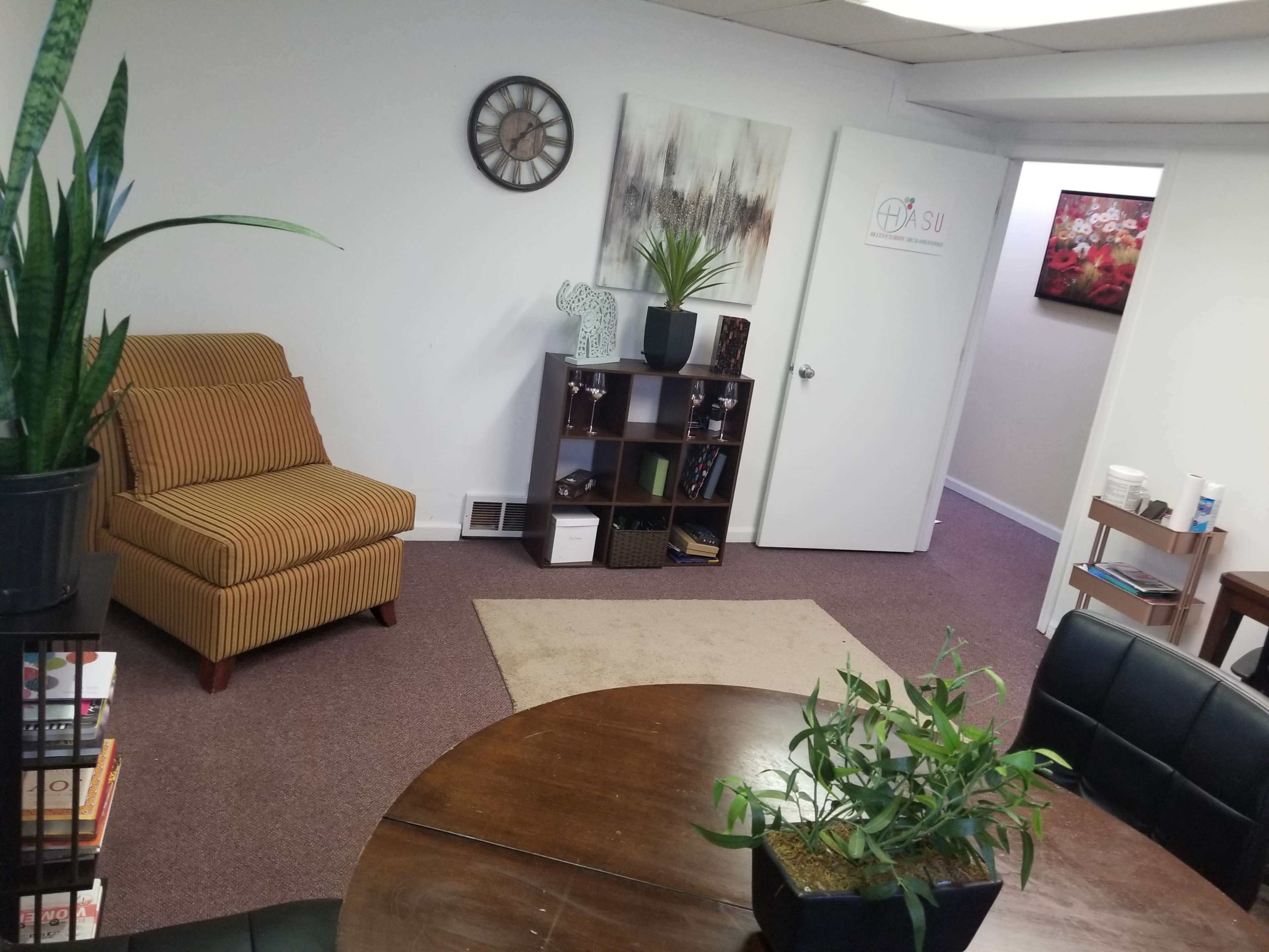 A well-lit office space featuring a striped chair, a bookshelf, a round table with plants, and decorative wall art.