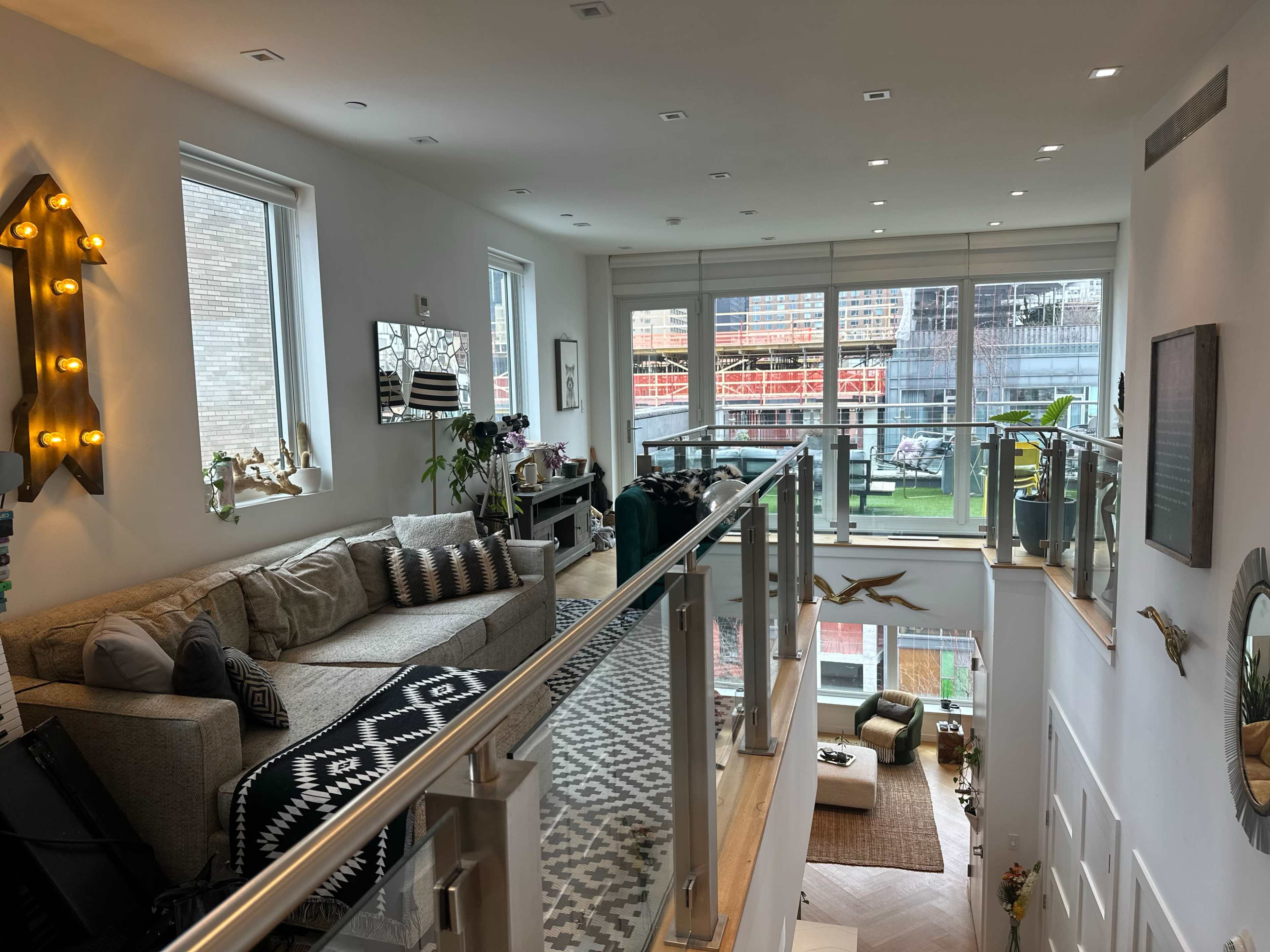 The image shows a modern, two-level living space with large windows, a comfortable sofa, and a view of a patio area outside.