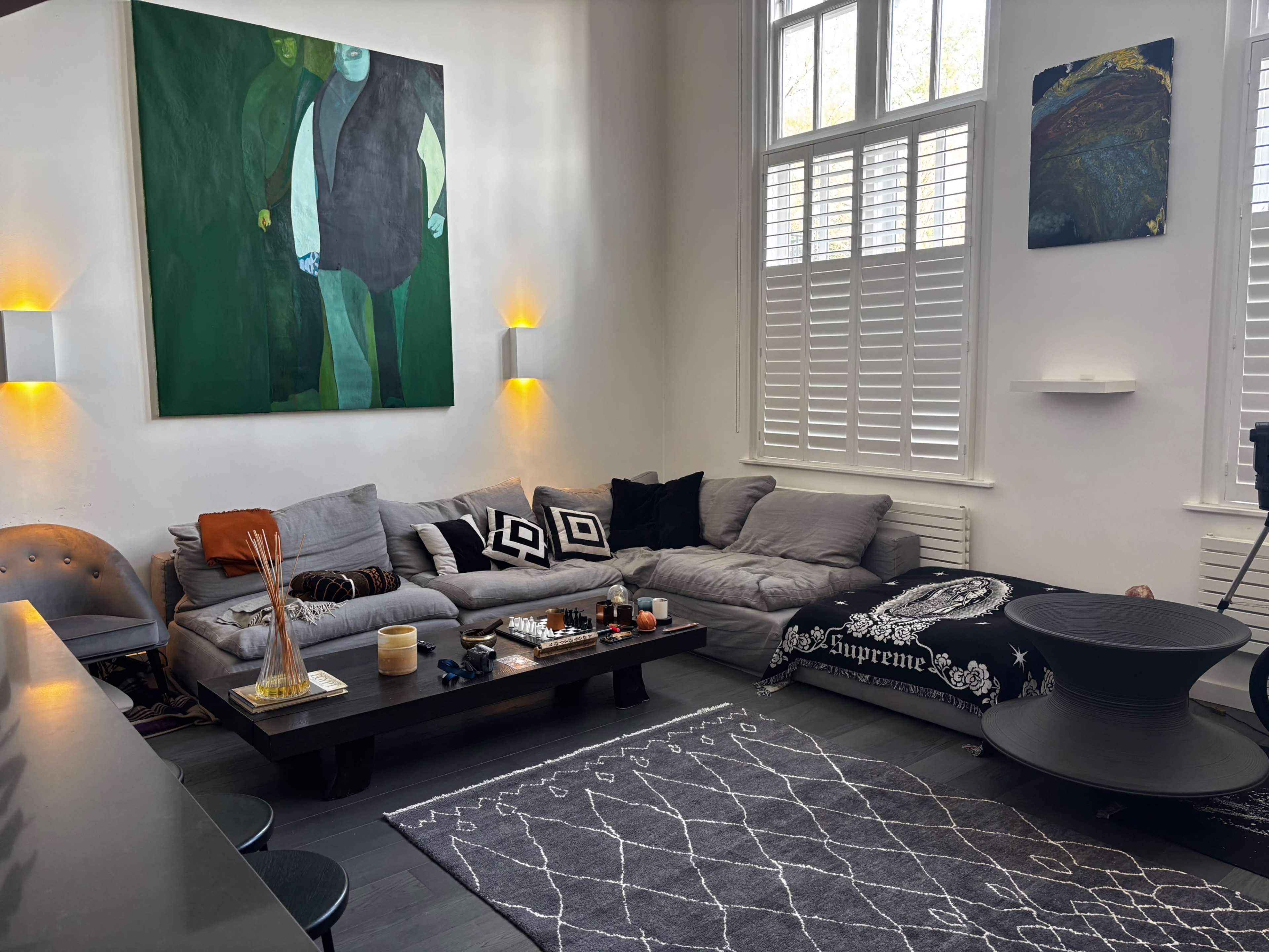 The image shows a modern living room with a gray sectional couch, a dark coffee table, and various decorative items, including artwork on the walls and a large area rug.
