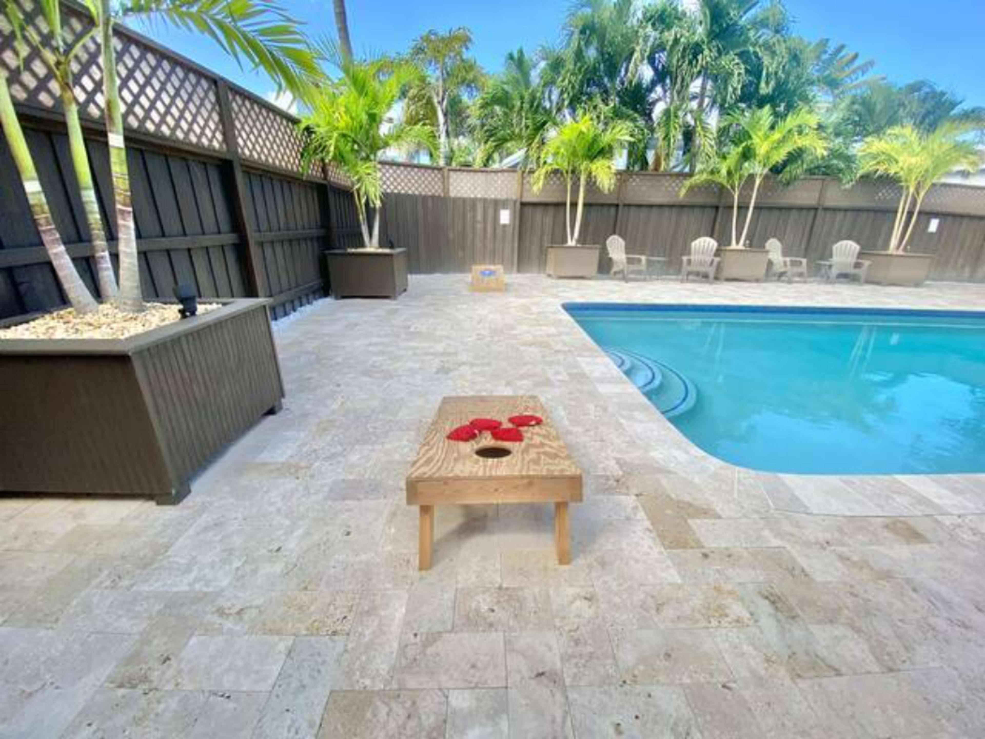 A wooden table with red decorations is placed near a swimming pool surrounded by palm trees and lounge chairs.