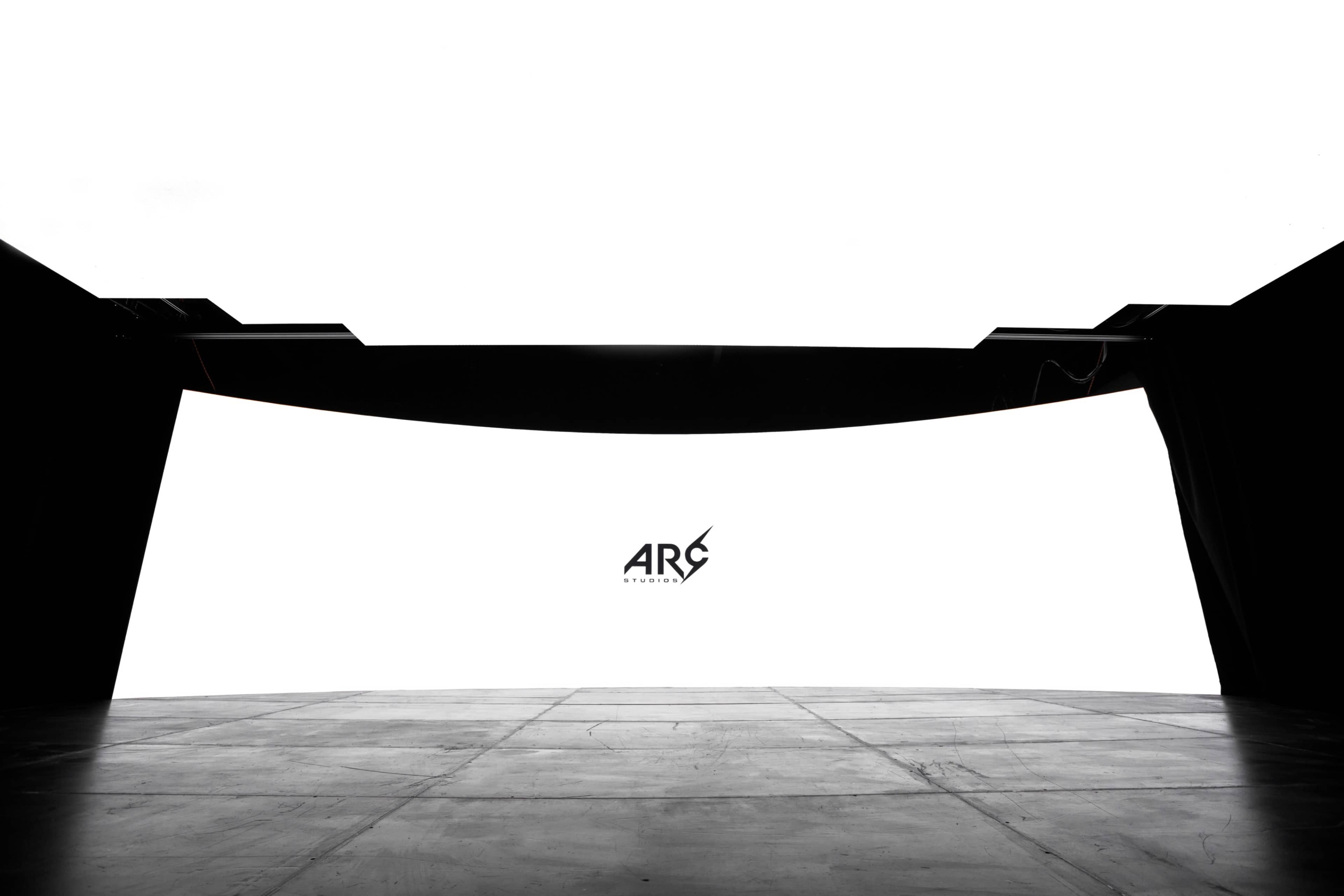 A minimalist stage with a large white backdrop and a logo centered in the foreground, flanked by dark, draped curtains.