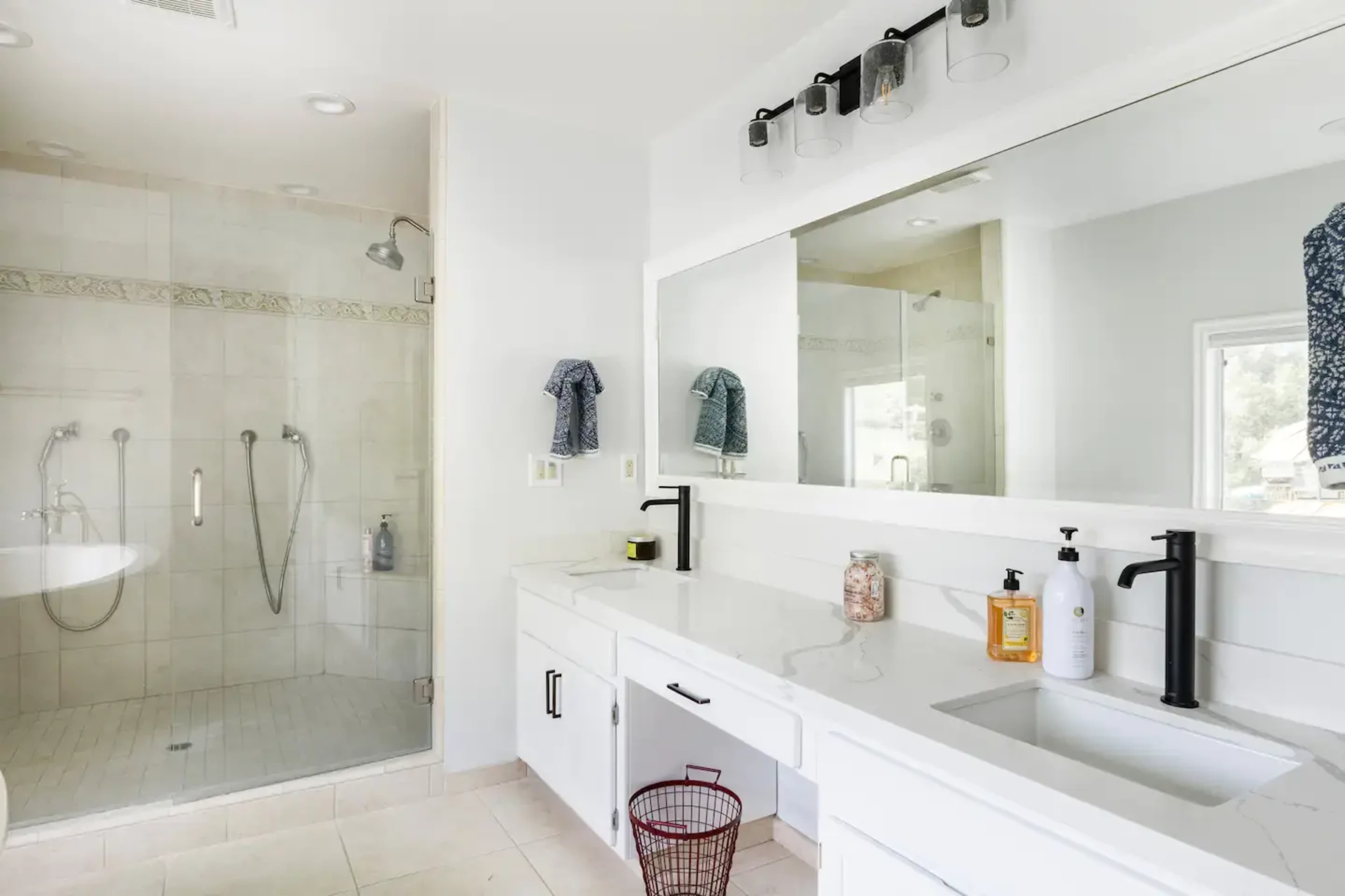 A modern bathroom with a glass shower, a large mirror above a double sink, and minimalistic cabinetry.