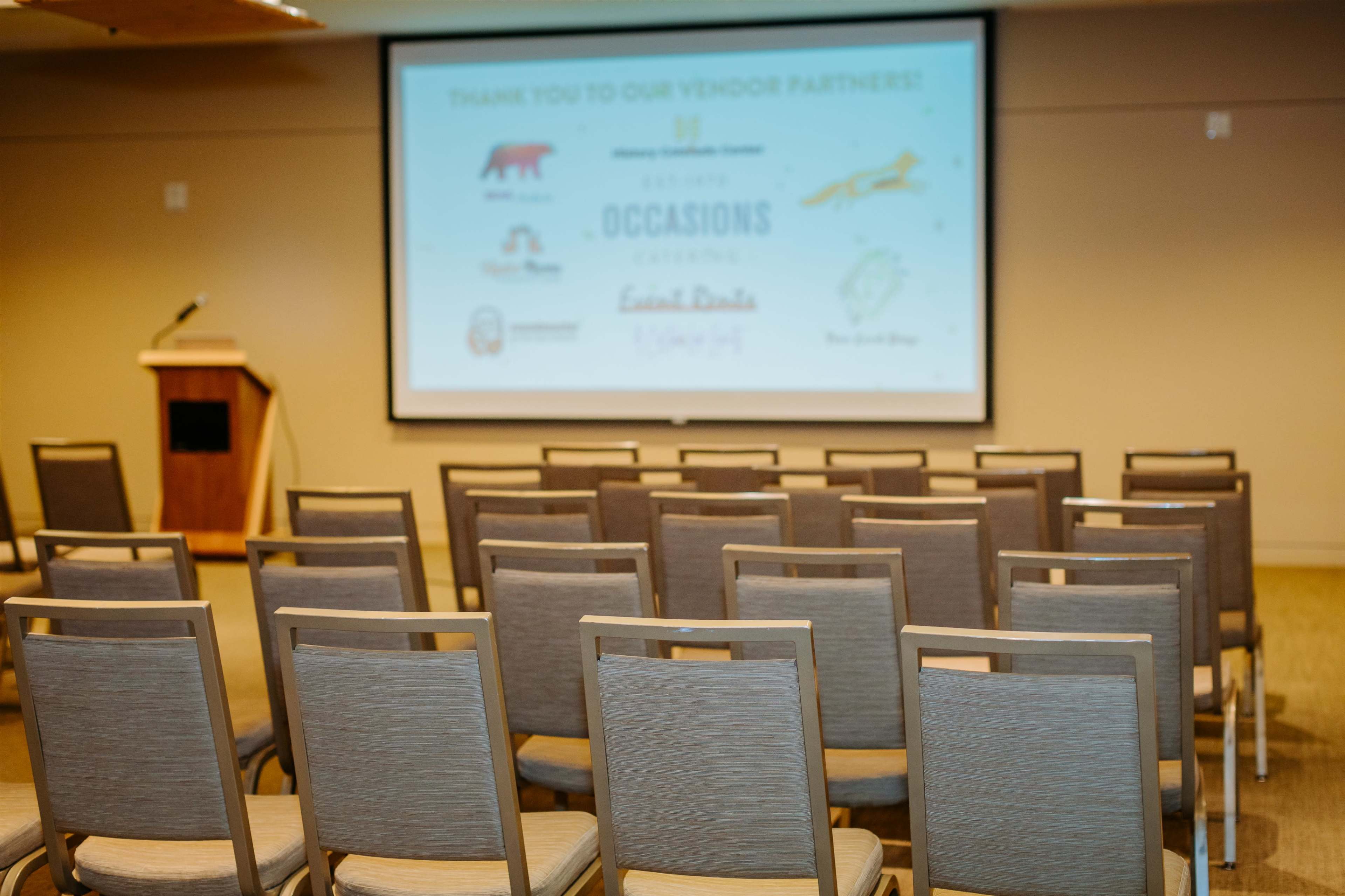 A conference room setup with rows of empty chairs facing a large screen displaying logos and a thank-you message to vendor partners.