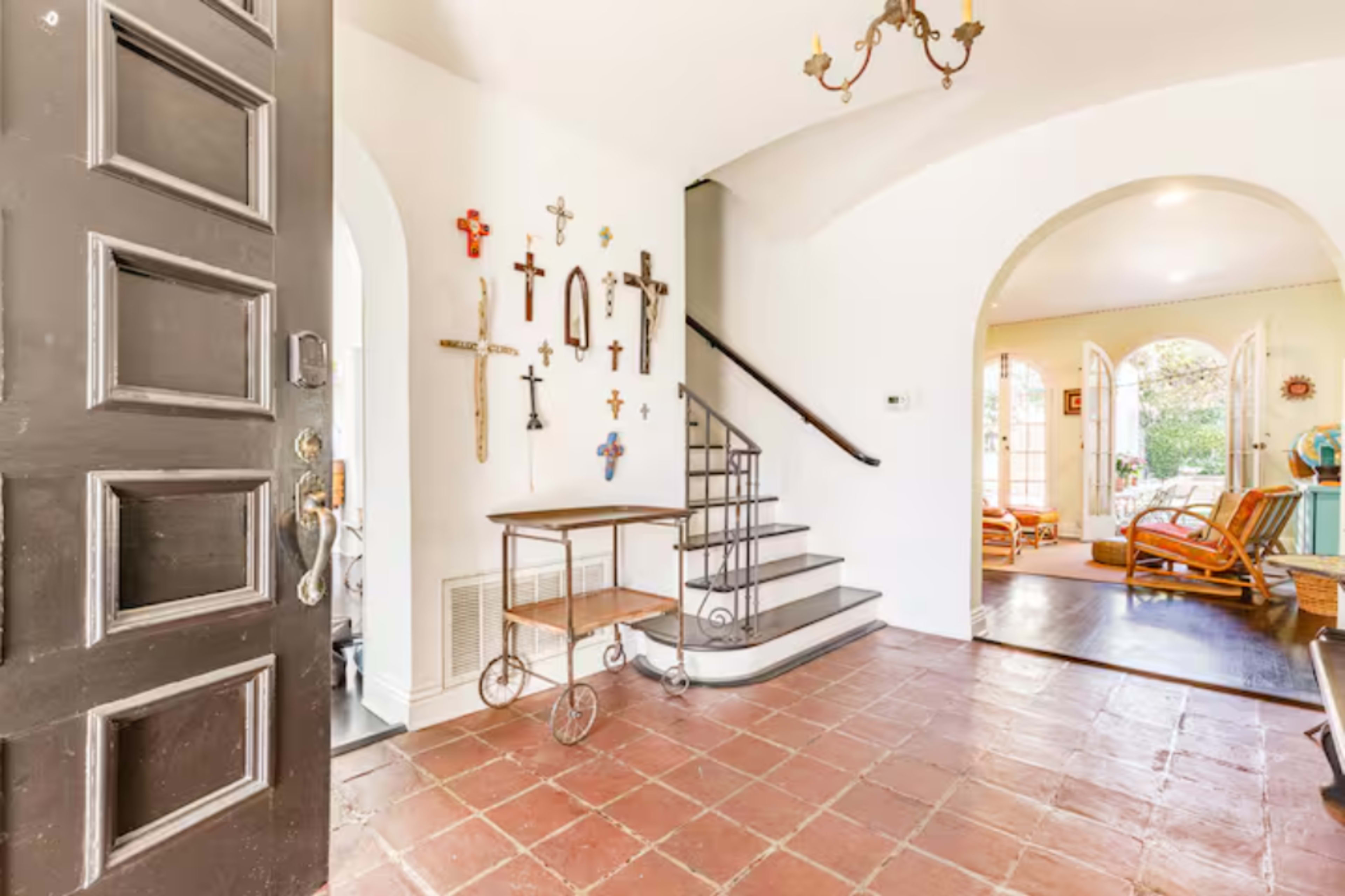 The entrance features a black door, a tiled floor, and a staircase beside a wall adorned with various crosses.