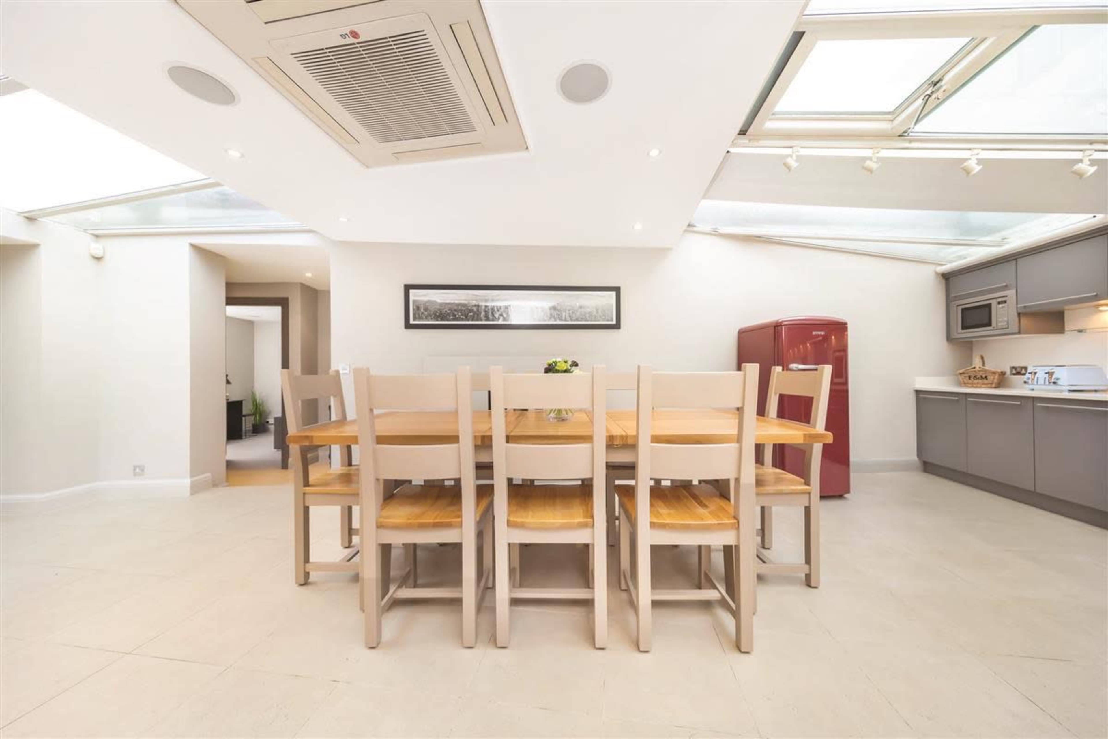 A spacious kitchen with a large wooden dining table and eight chairs is illuminated by natural light from the skylights above.