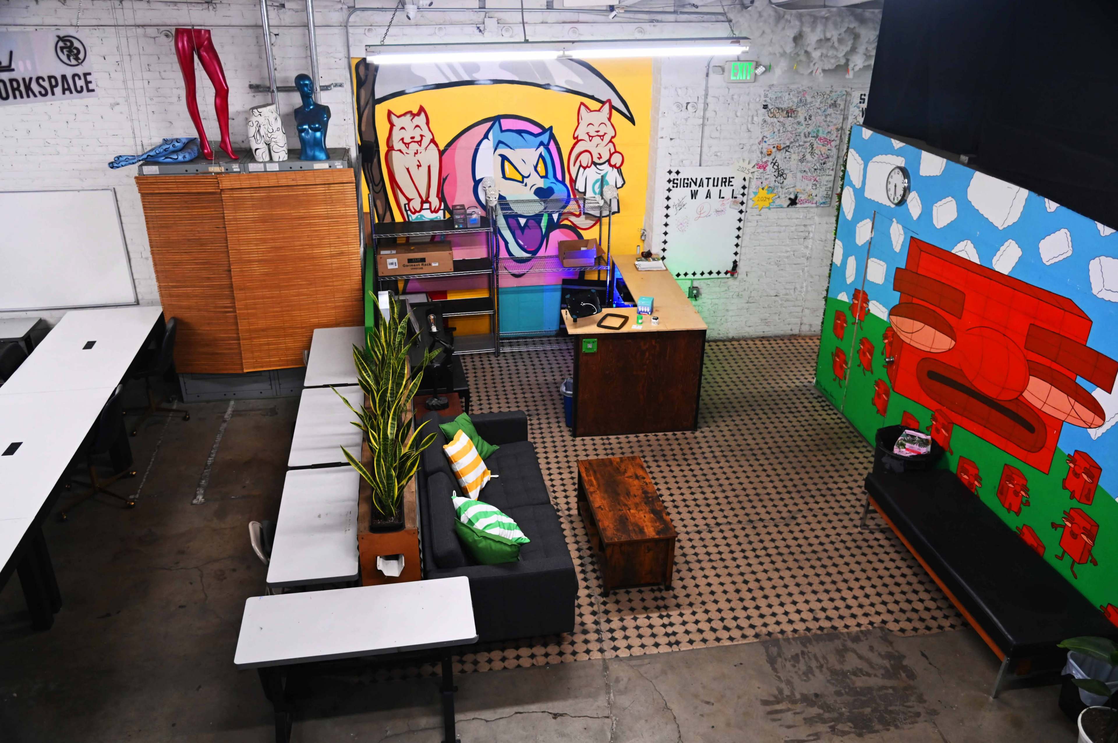 The image shows a vibrant workspace with colorful wall art, seating areas, and tables arranged for collaboration.