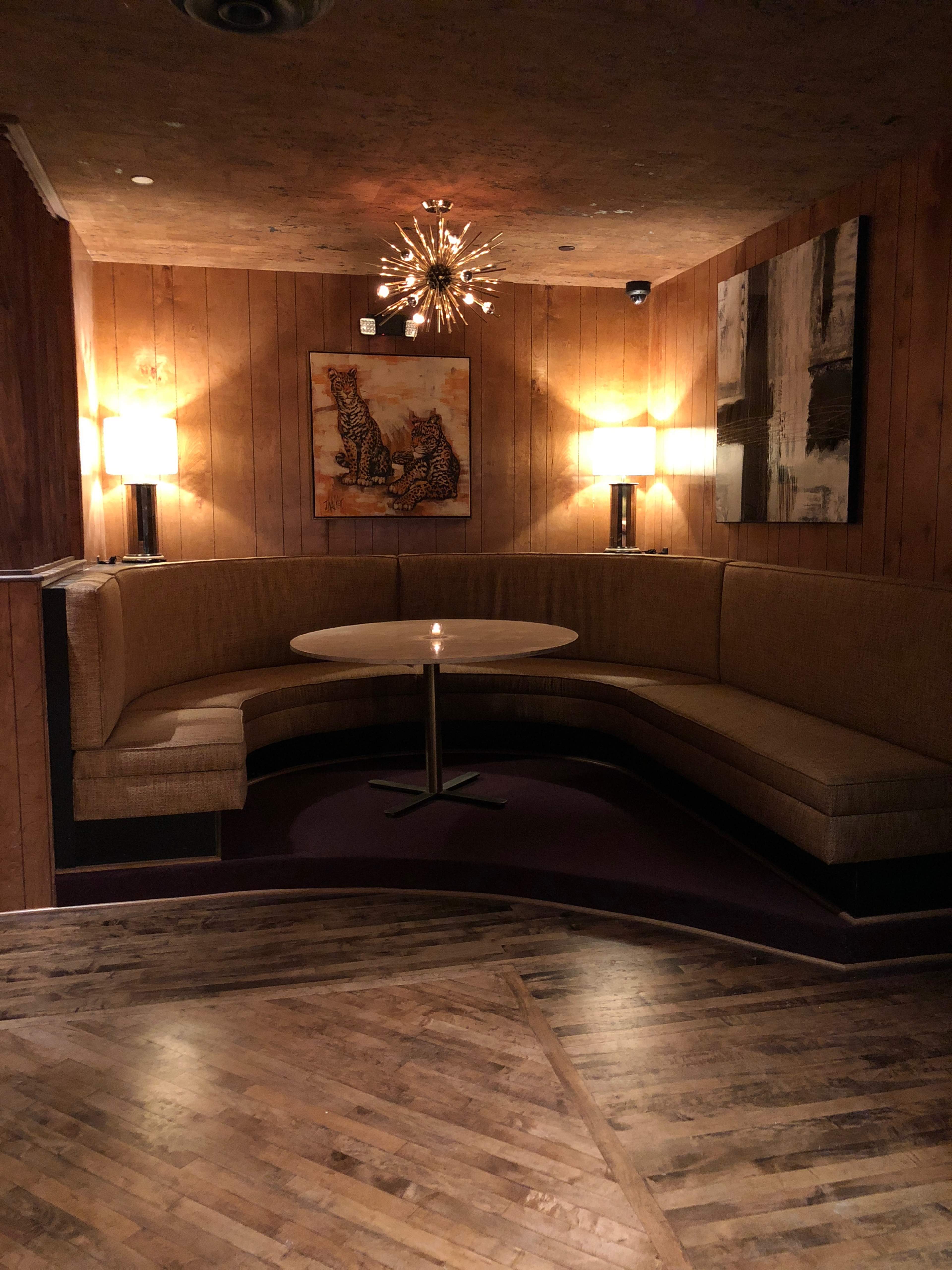 A cozy seating area features a circular table surrounded by a curved bench, illuminated by wall lamps and a central hanging light fixture.