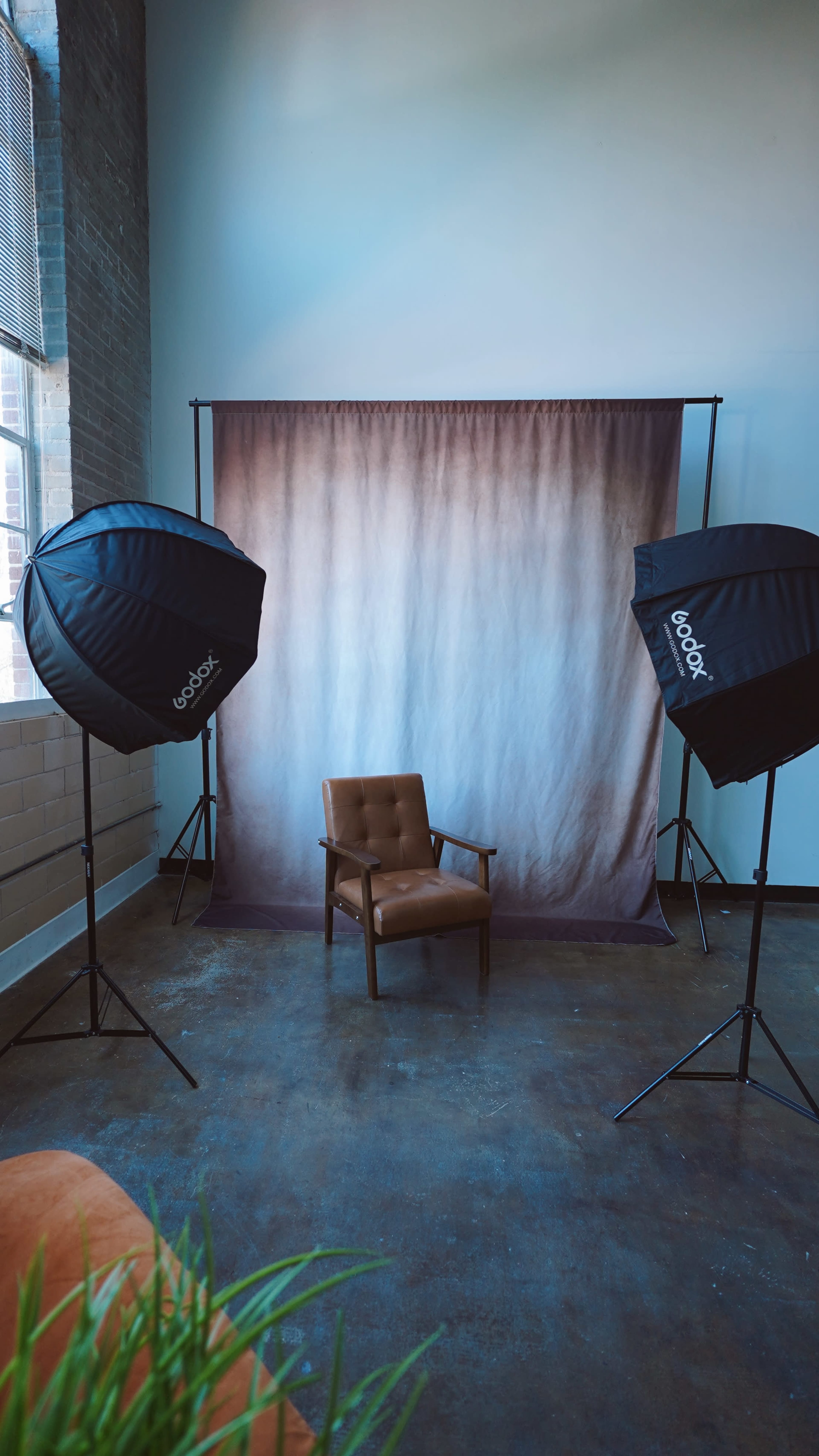 The image shows a photo studio setup with a wooden chair positioned in front of a gradient backdrop, flanked by two large softbox lights.