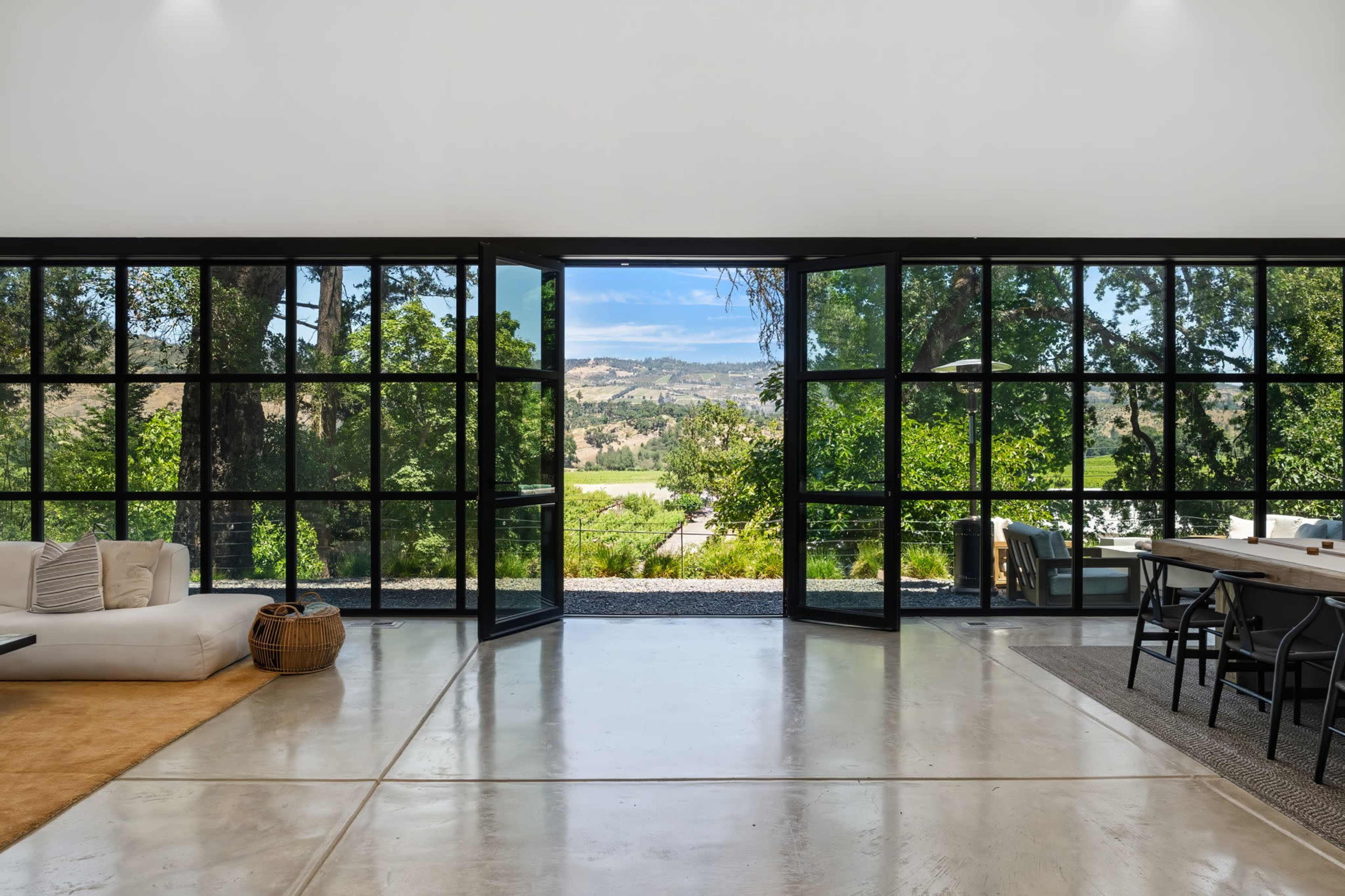 The image shows a spacious interior with large glass doors opened to a scenic view of rolling hills and trees.
