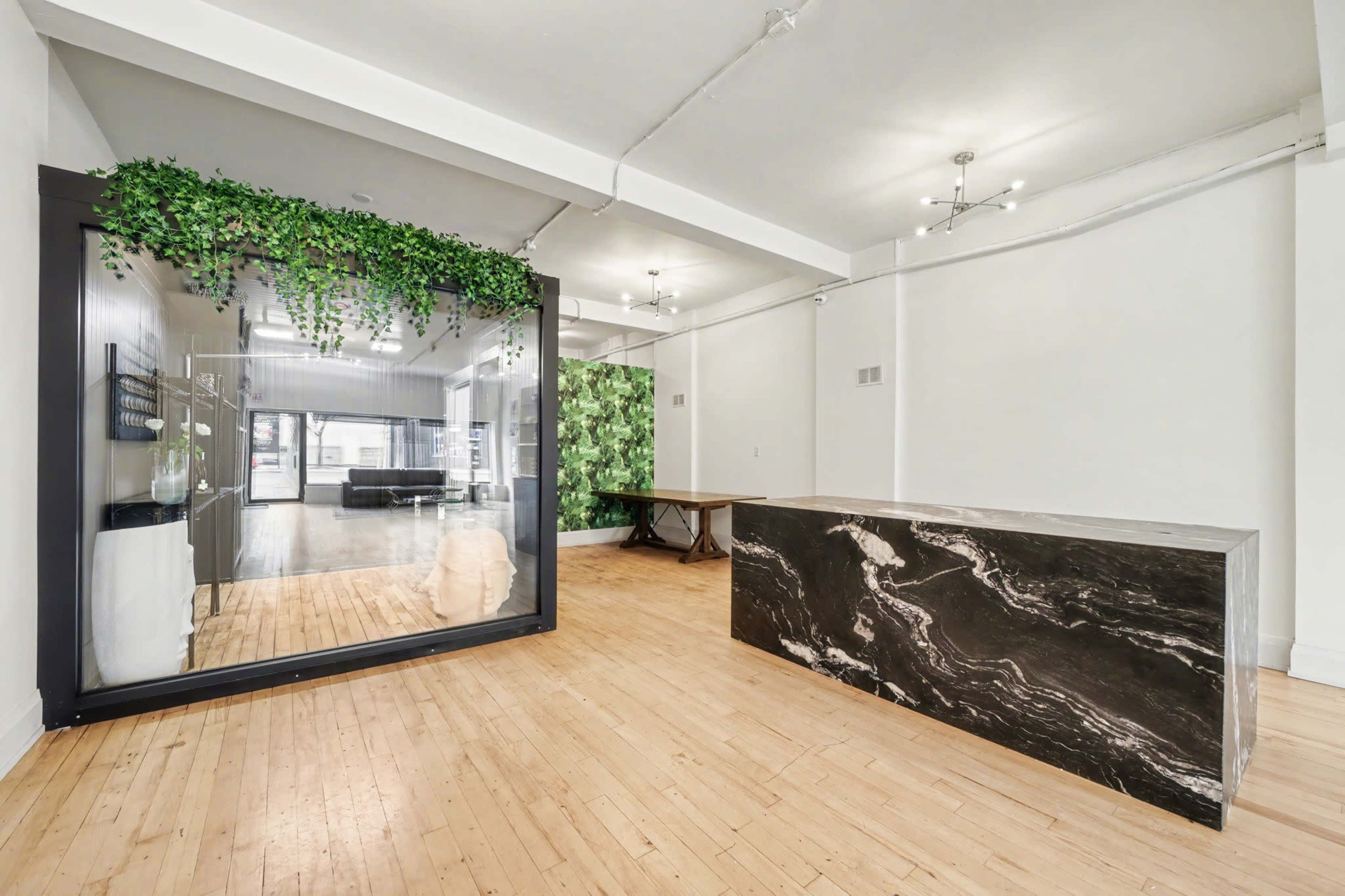 The image shows a modern office space with a glass-walled meeting area decorated with greenery and a large marble reception desk.