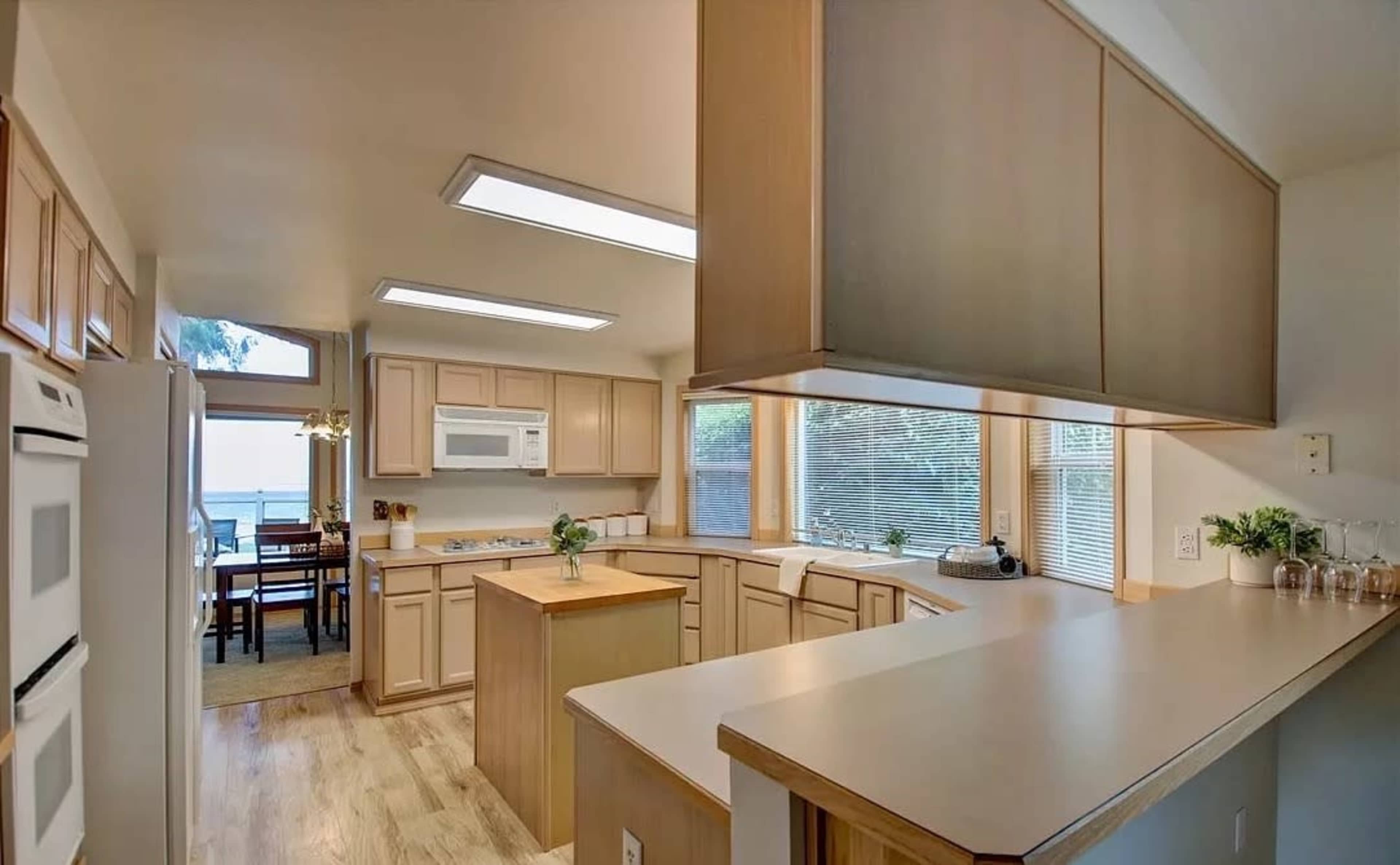 A spacious kitchen features wooden cabinetry, a central island, and large windows allowing natural light to enter.