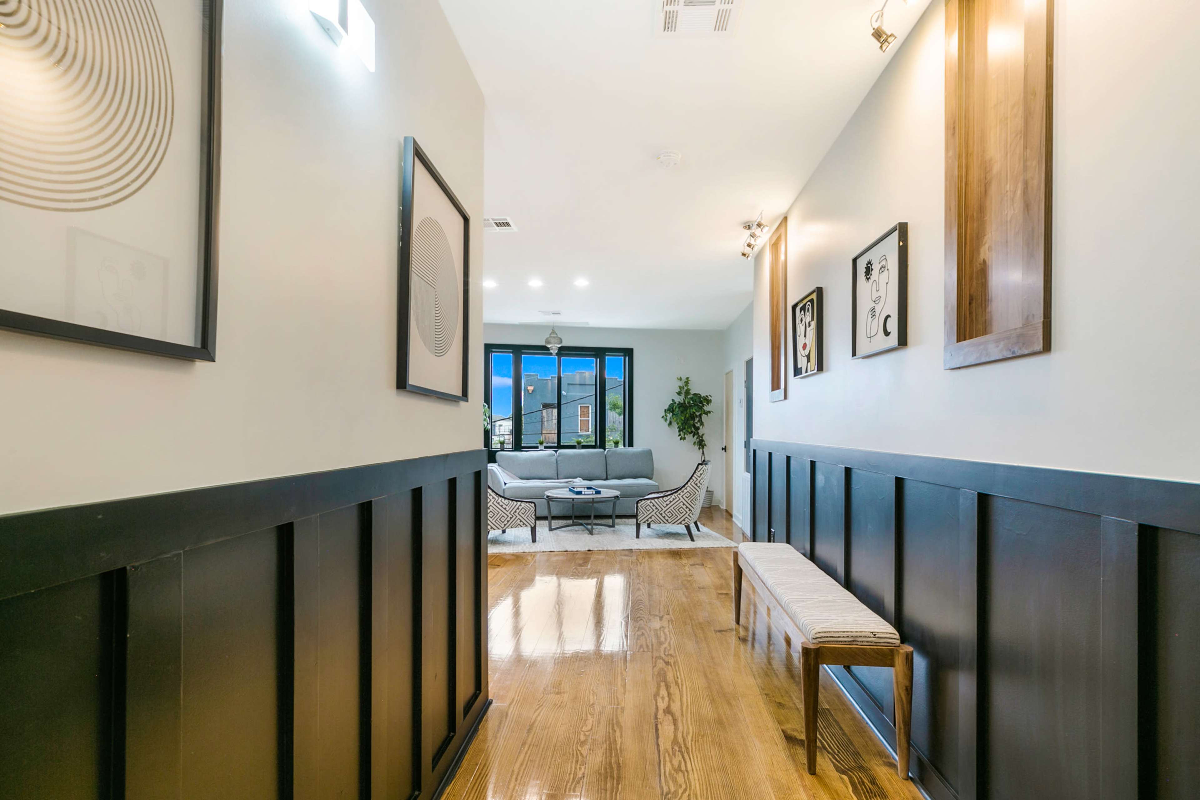 A long hallway with black paneling leads to a living area featuring a gray sofa and decorative wall art.