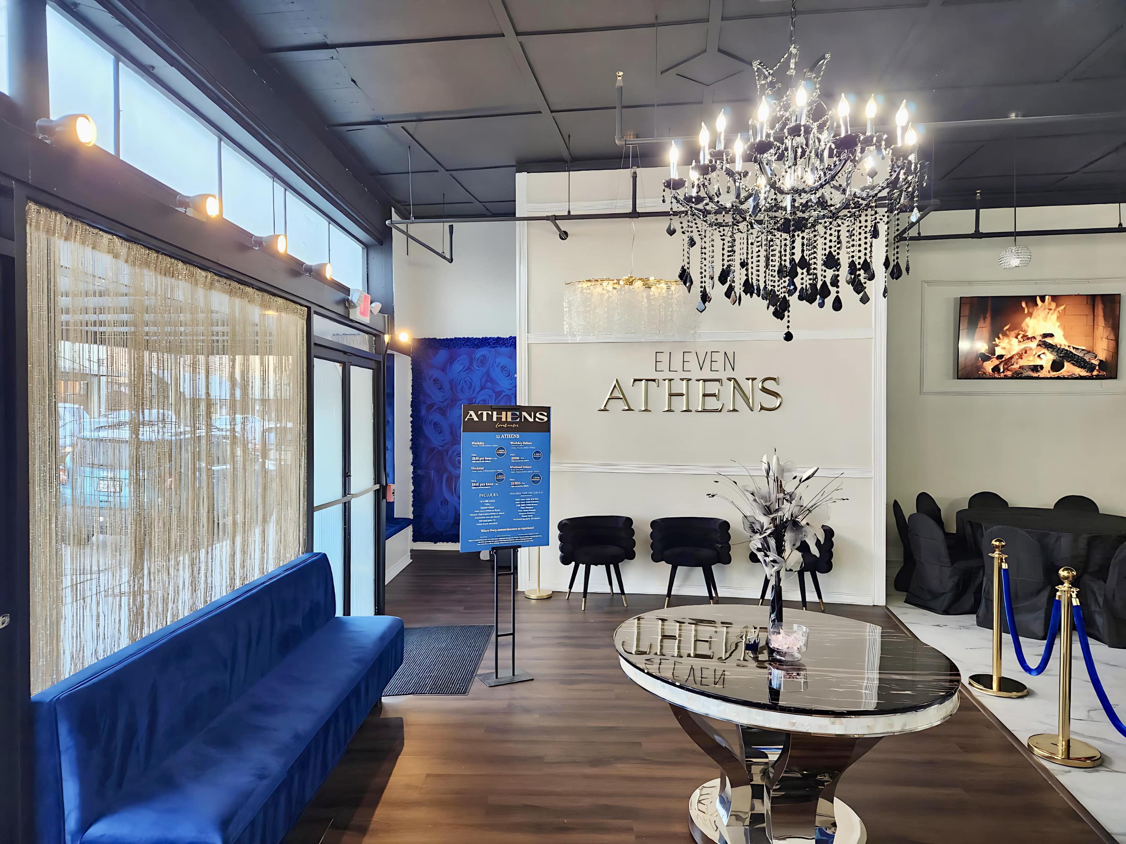 The image shows the interior of a stylish establishment named "Eleven Athens," featuring a blue velvet seating area, a modern chandelier, and a decorative table in front of a sign on the wall.