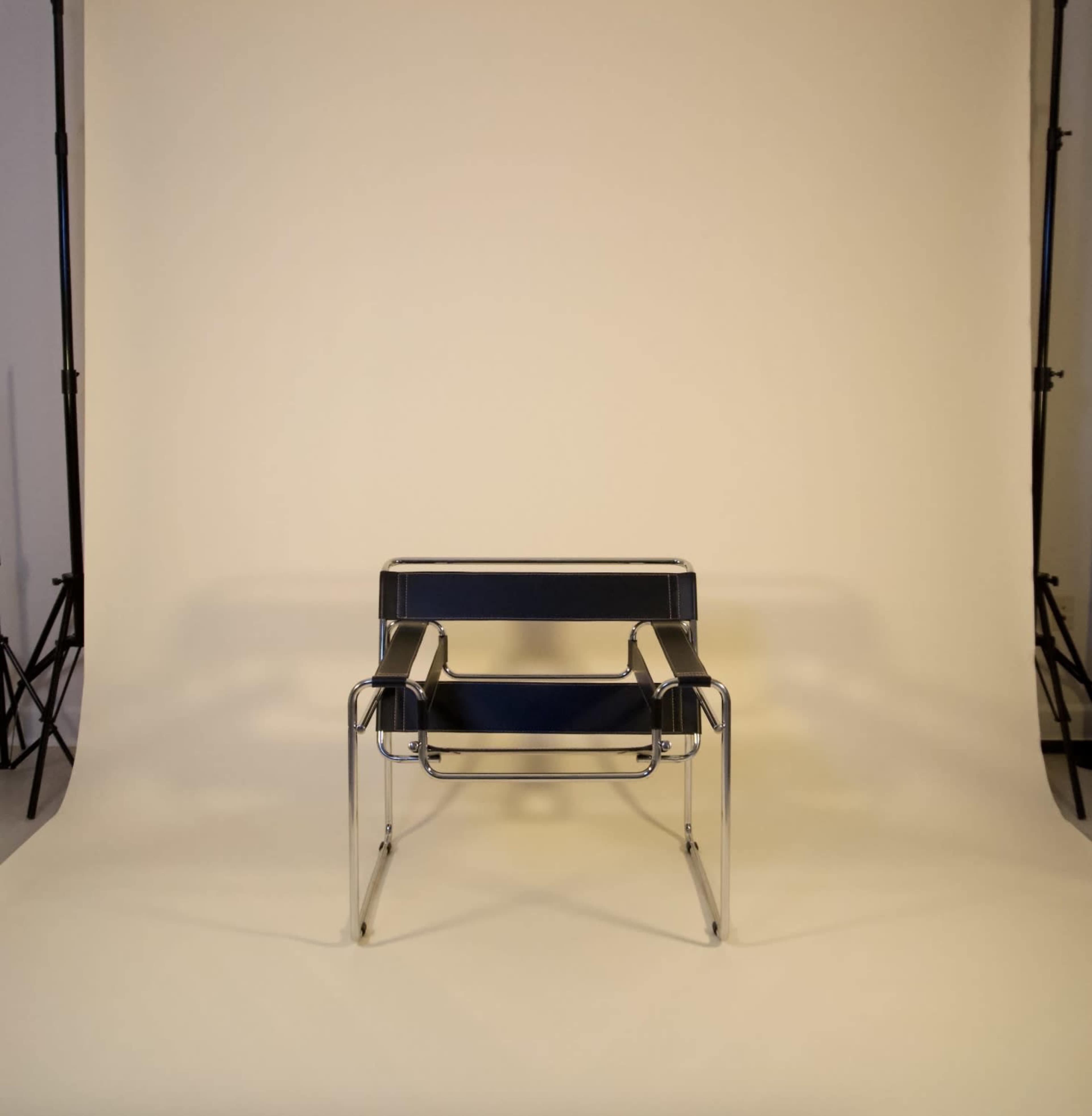 A modern chair with a chrome frame and blue seat and backrest is centered against a plain light backdrop.