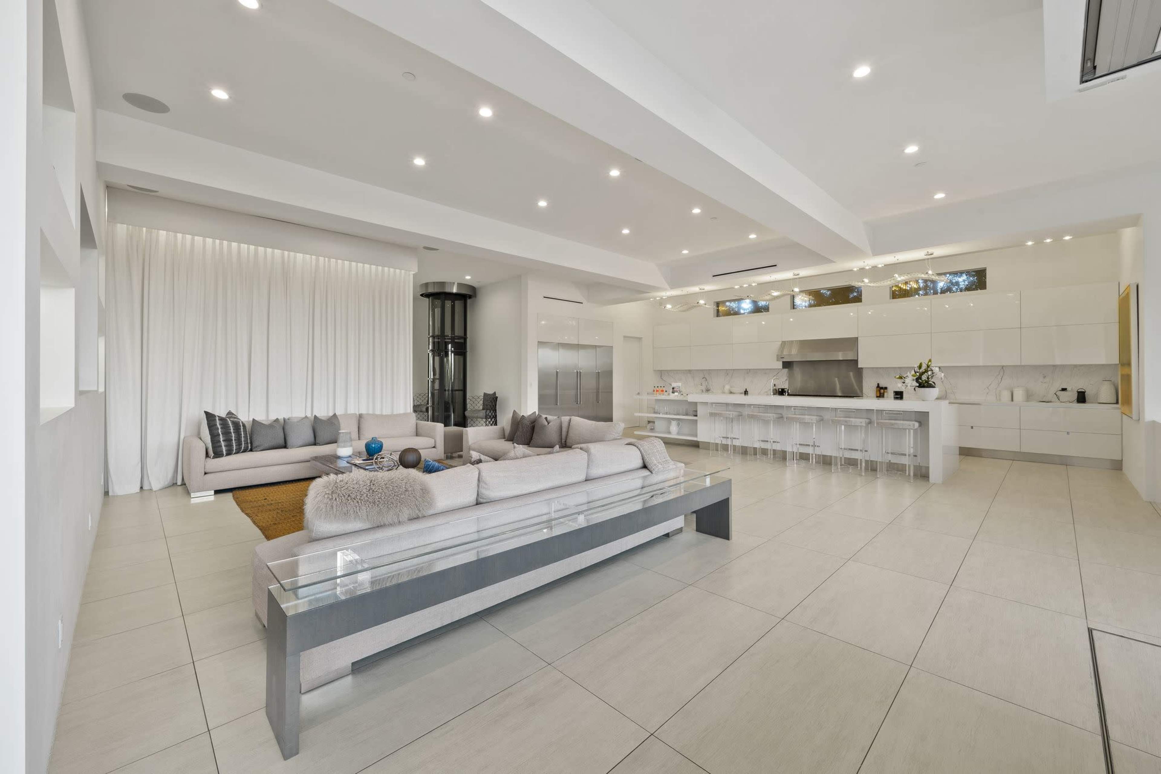 A modern open-concept living space featuring a large sectional sofa, sleek kitchen cabinets, and a minimalist design with ample natural light.