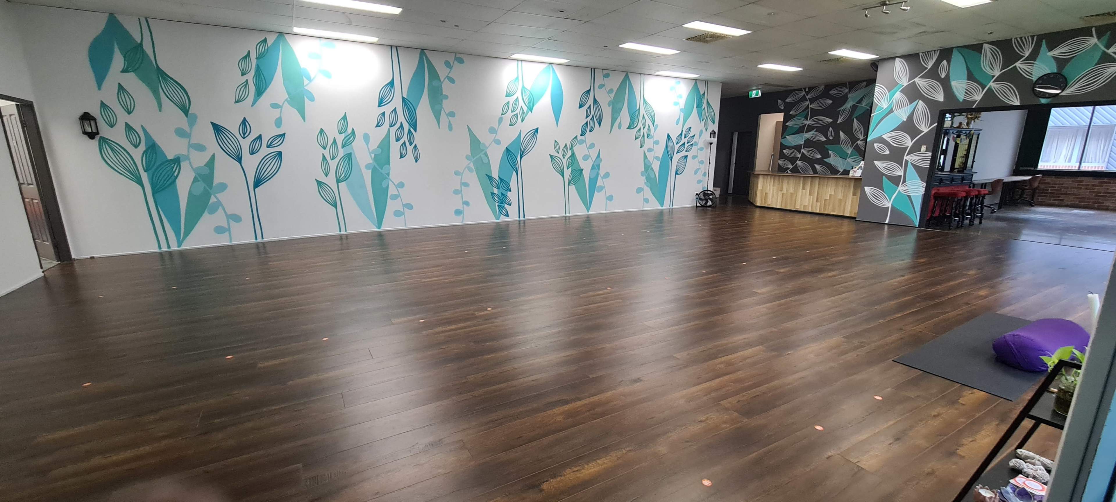 The image shows a spacious room with wooden flooring and walls decorated with blue and green leaf patterns.