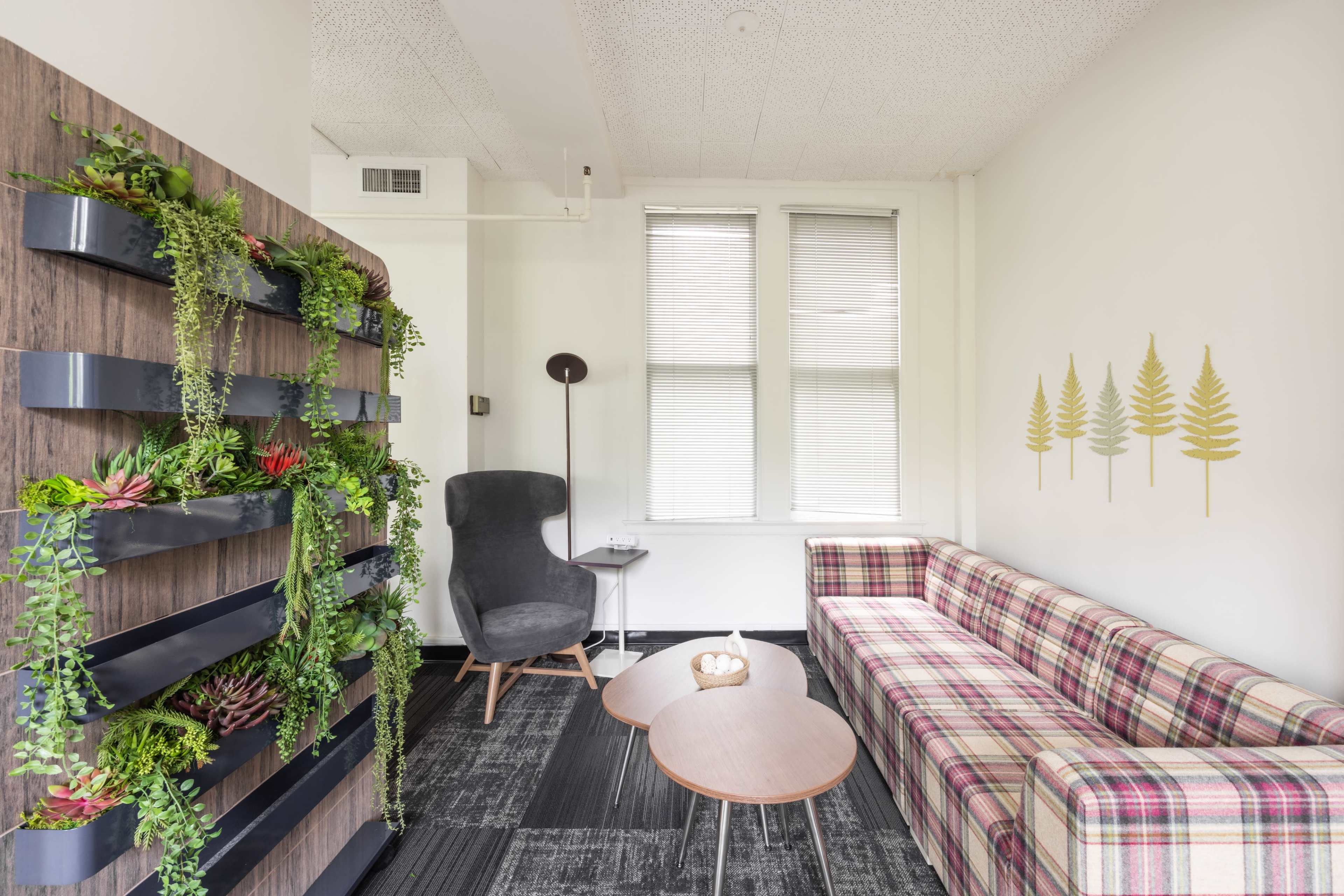 A small lounge area features a plaid sofa, wooden side tables, a modern chair, and a wall adorned with vertical planters.