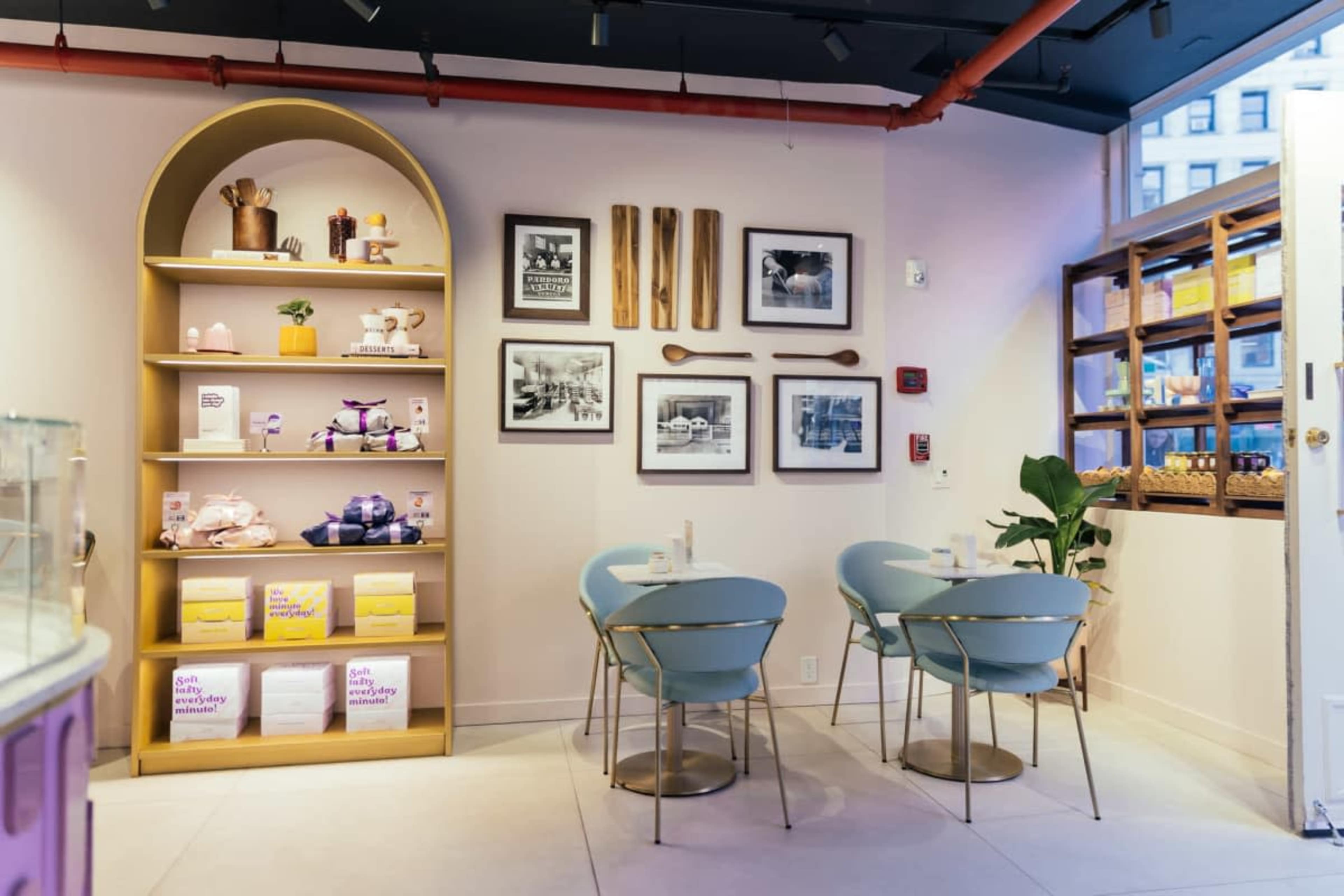 The image shows a stylish café interior featuring a wooden display shelf, framed black-and-white photographs on the walls, and blue chairs around small tables.
