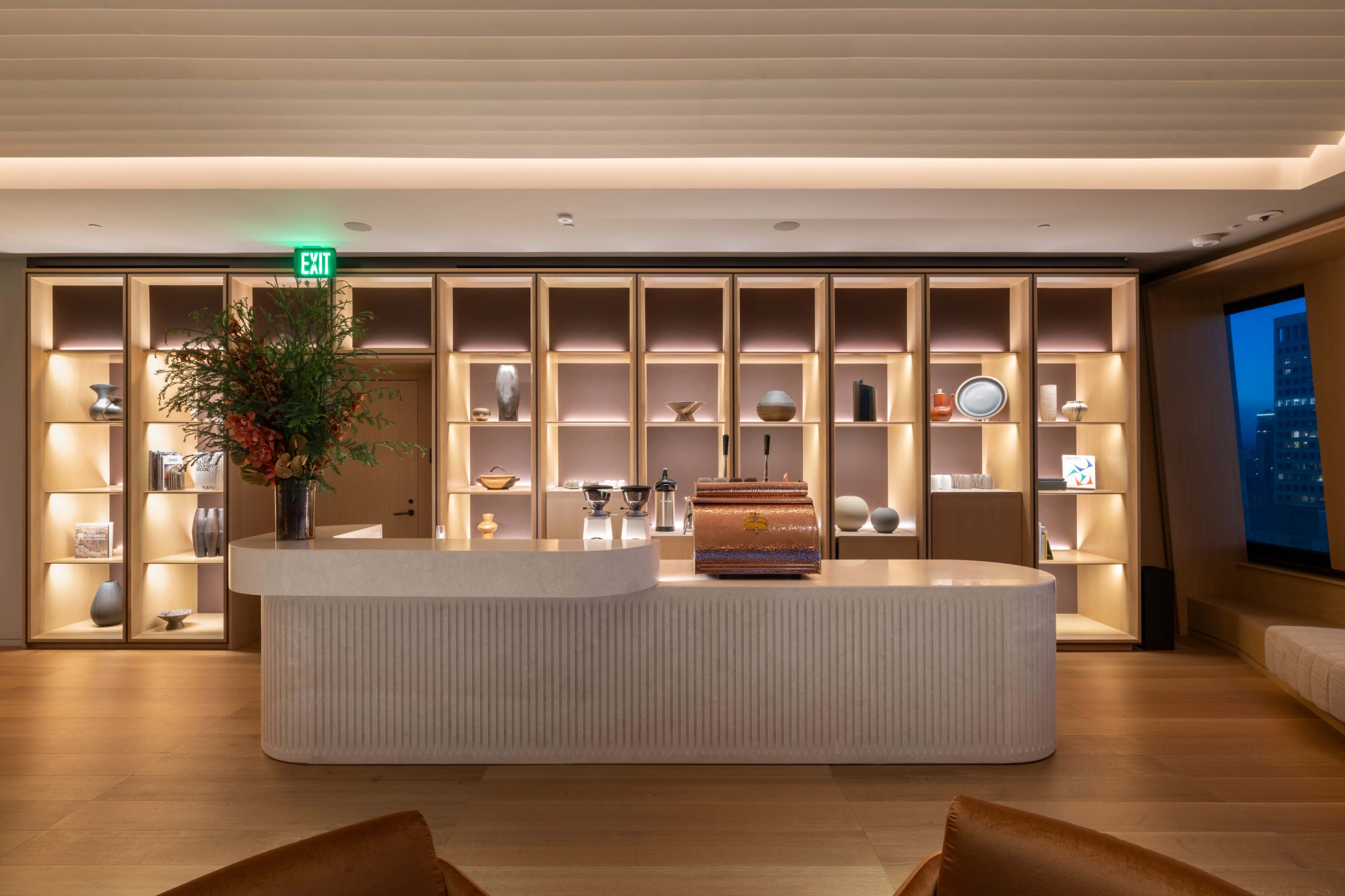 The image shows a modern reception area with a curved white counter and neatly arranged shelving displaying various decorative objects.
