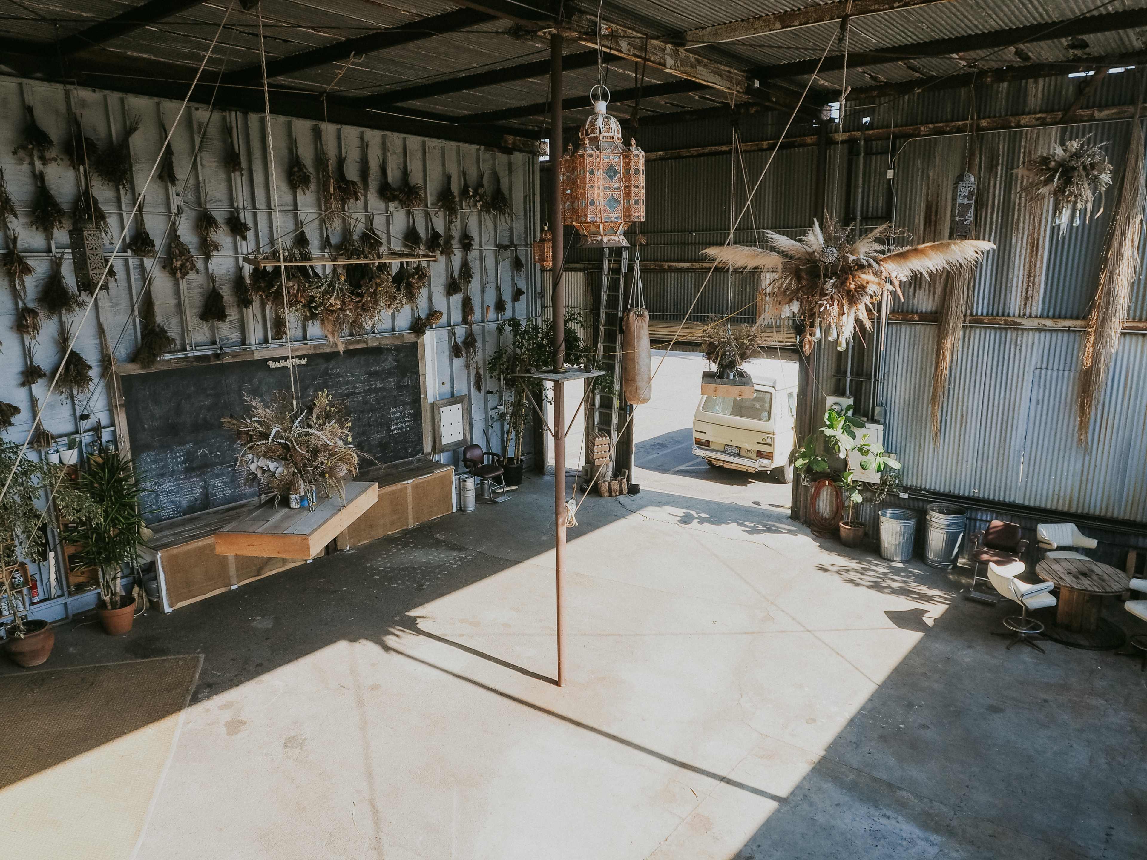 A spacious warehouse with plants and decorative items suspended from the ceiling, along with a small vehicle parked outside.