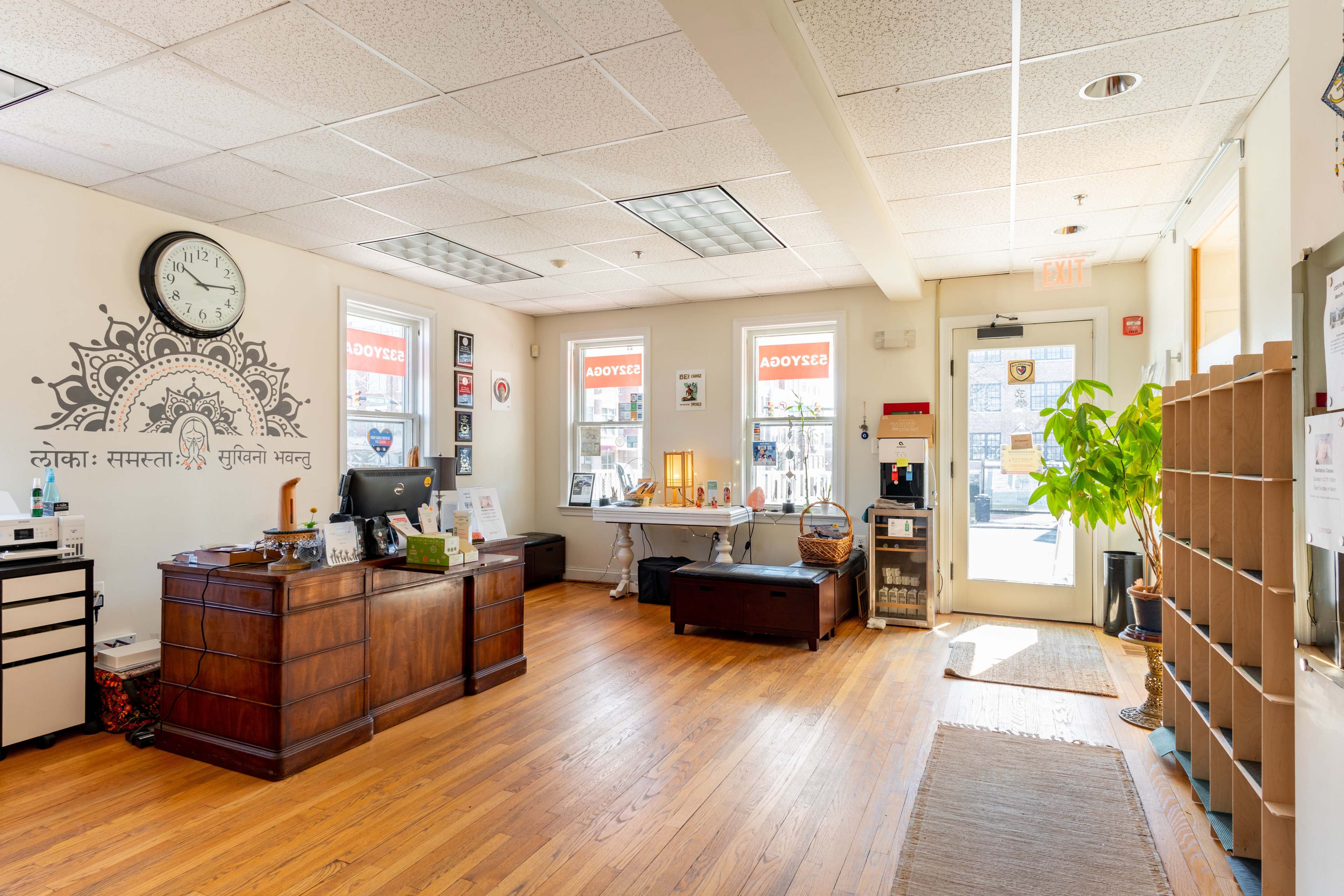 The interior of a welcoming office features a wooden desk, a large clock on the wall, and a door leading outside, with windows showcasing "ADOPT" signs.