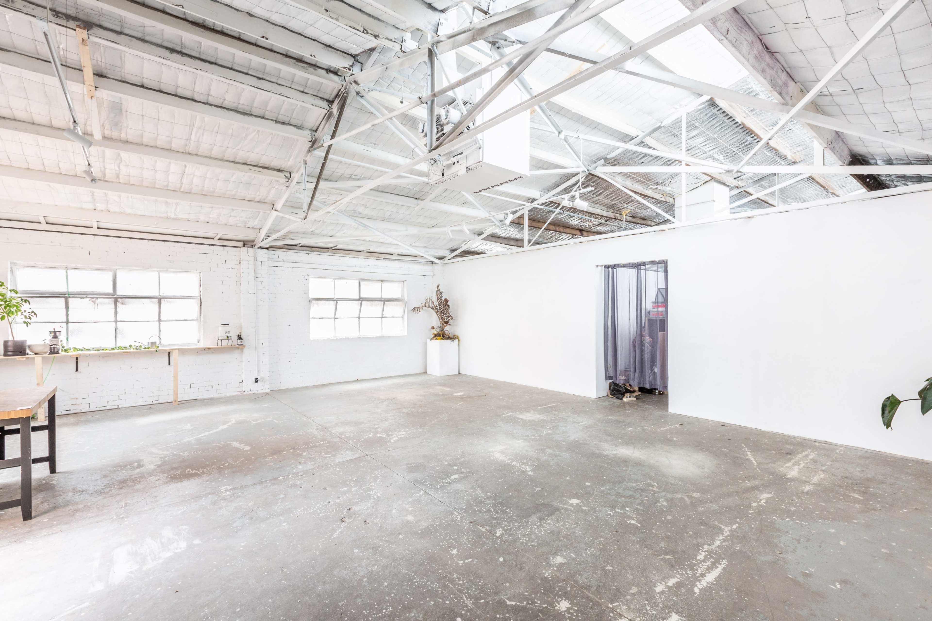An empty, industrial-style room with high ceilings, large windows, and a concrete floor.
