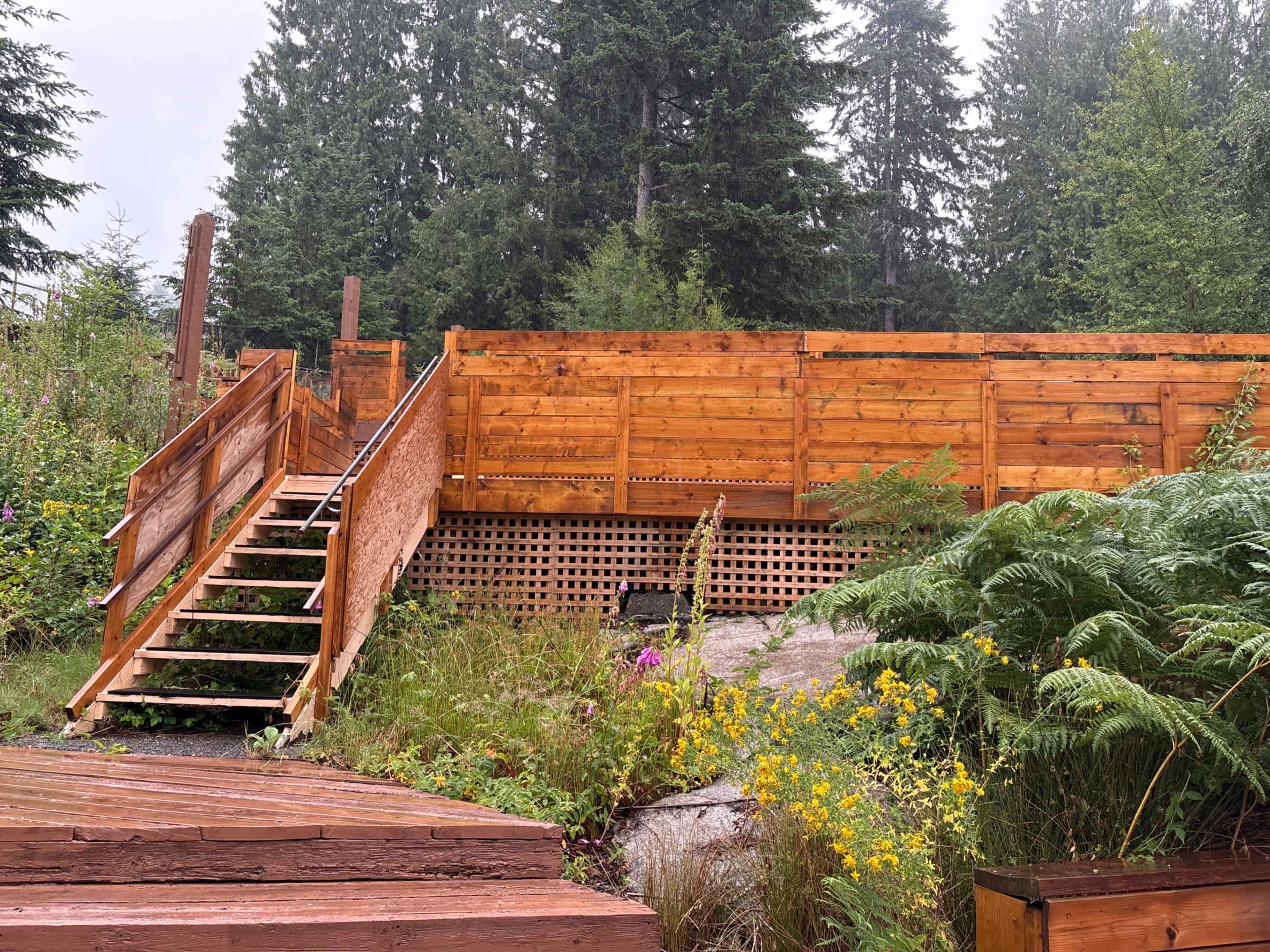 A wooden staircase leads up to a fenced area surrounded by trees and wildflowers.