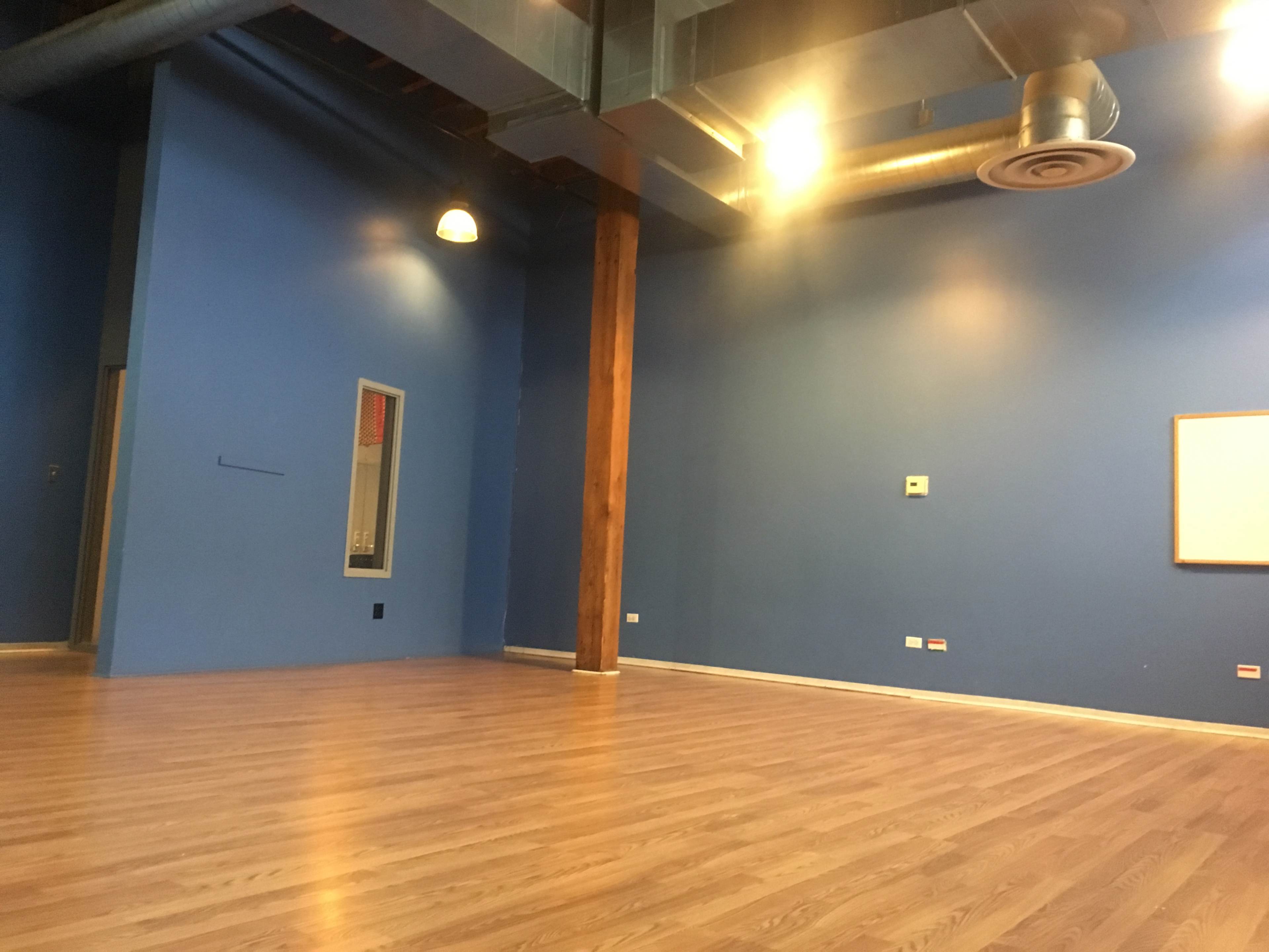 An empty room with blue walls, wooden flooring, and a large window along with a blank whiteboard on one wall.
