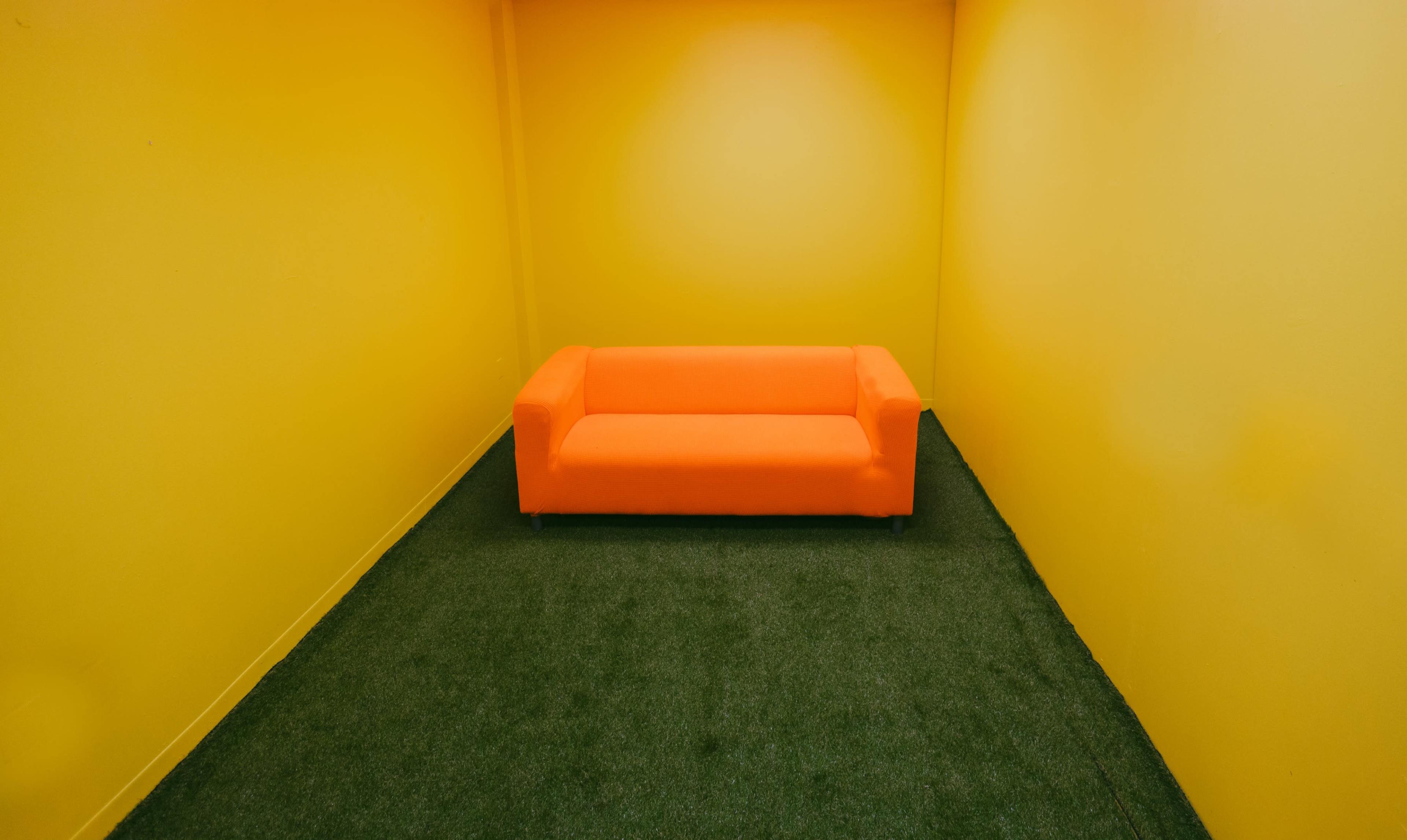 An orange couch is positioned in a small room with yellow walls and green carpet.