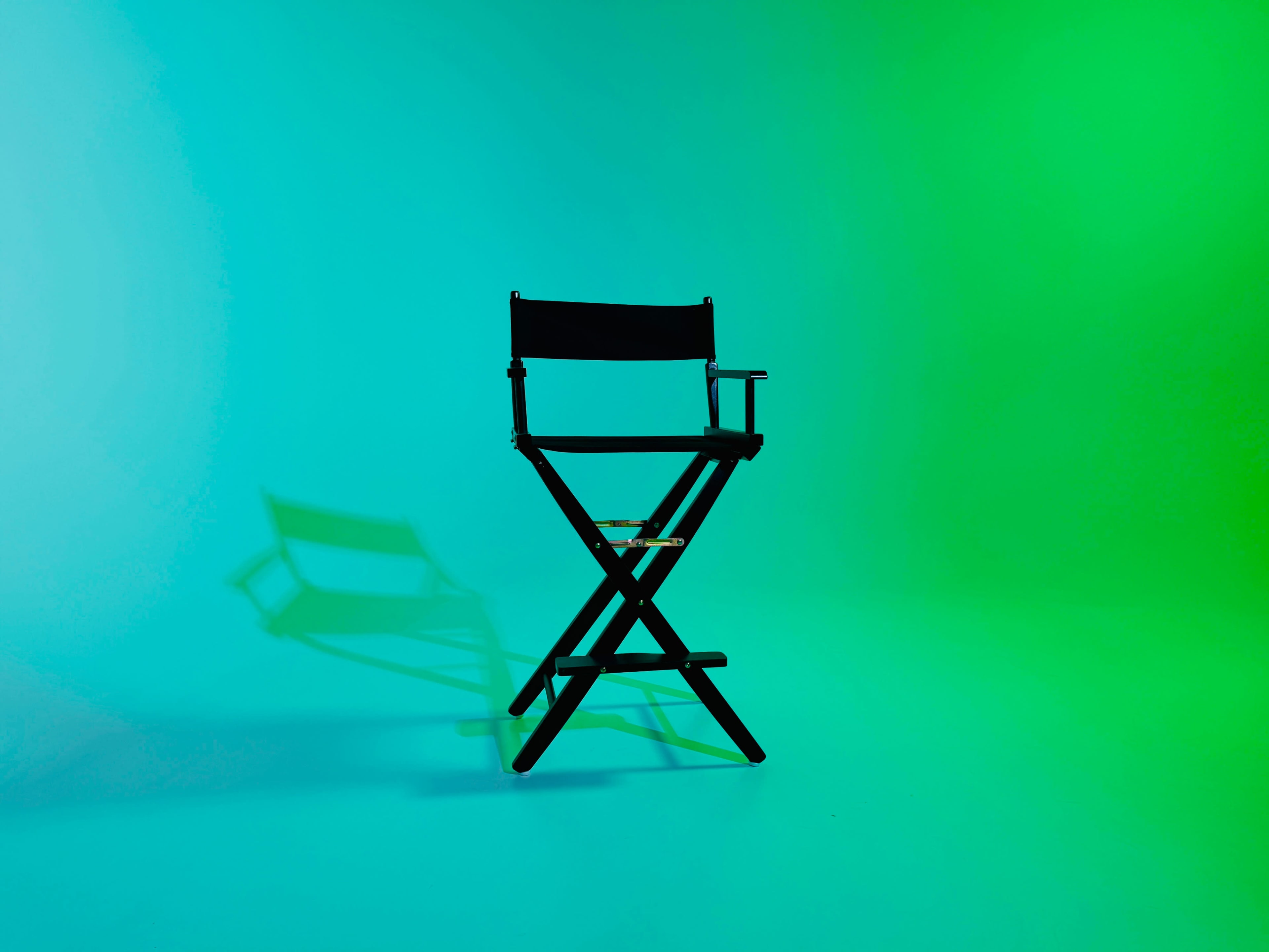 A black director's chair is positioned in front of a gradient background that transitions from blue to green.