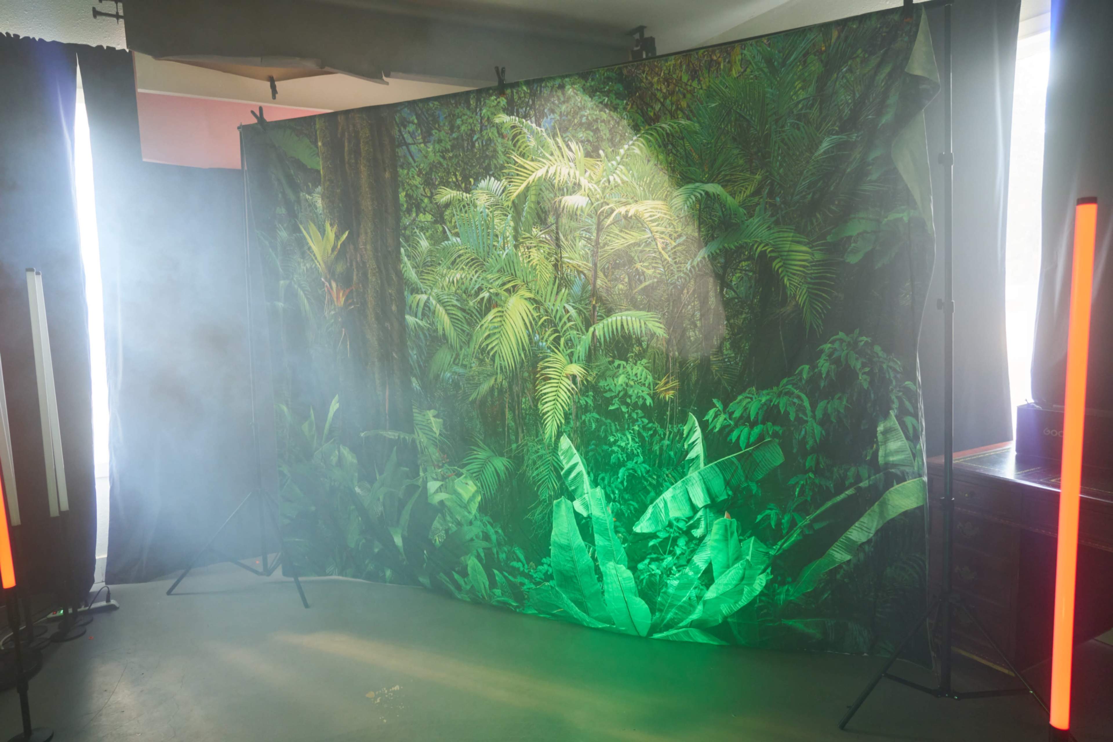 A large backdrop featuring a dense green jungle scene is set up in a space with soft fog and ambient lighting.