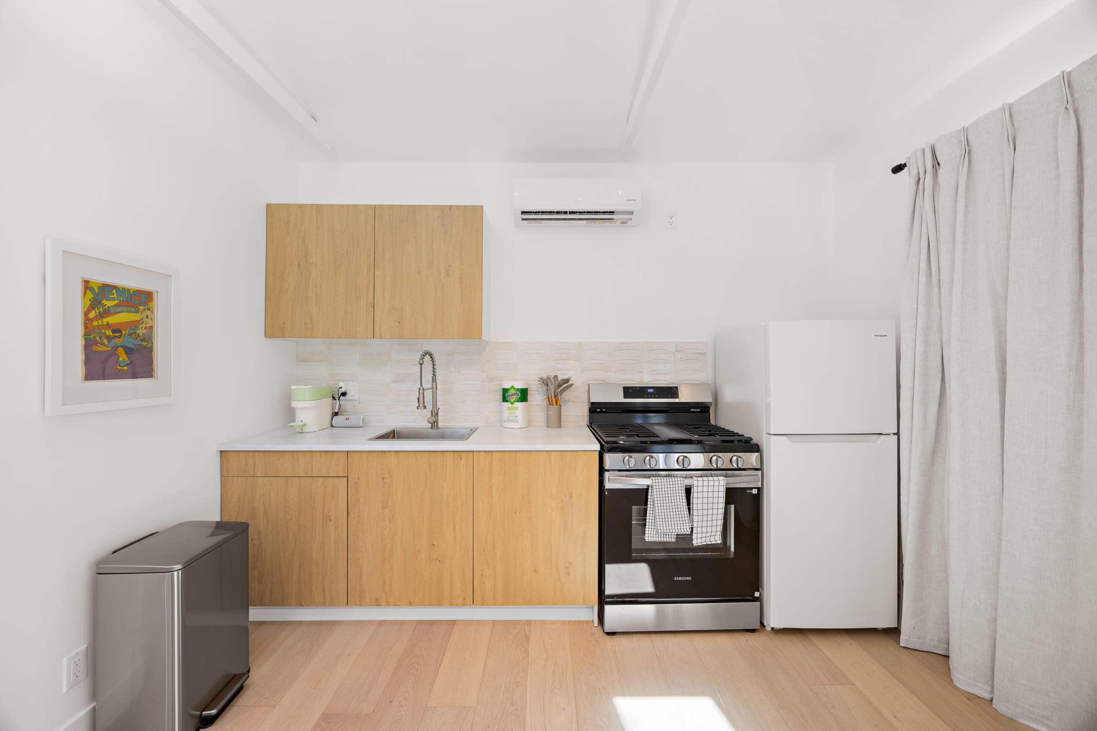 The image shows a modern kitchen with wooden cabinets, a stainless steel stove, a refrigerator, and a countertop with a sink.