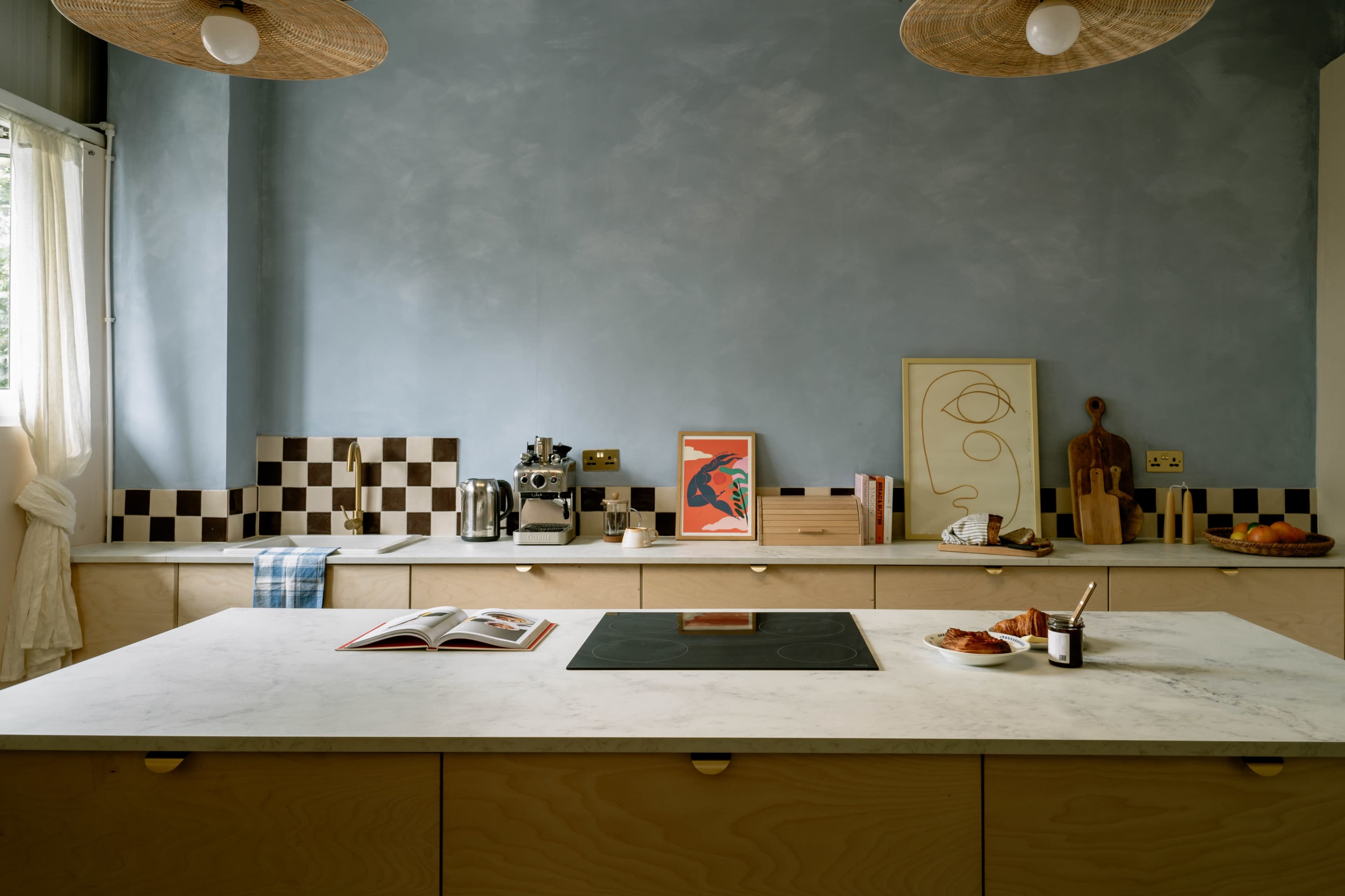 A modern kitchen features a central marble island, checkered backsplash, and an array of cooking utensils displayed on the countertops.