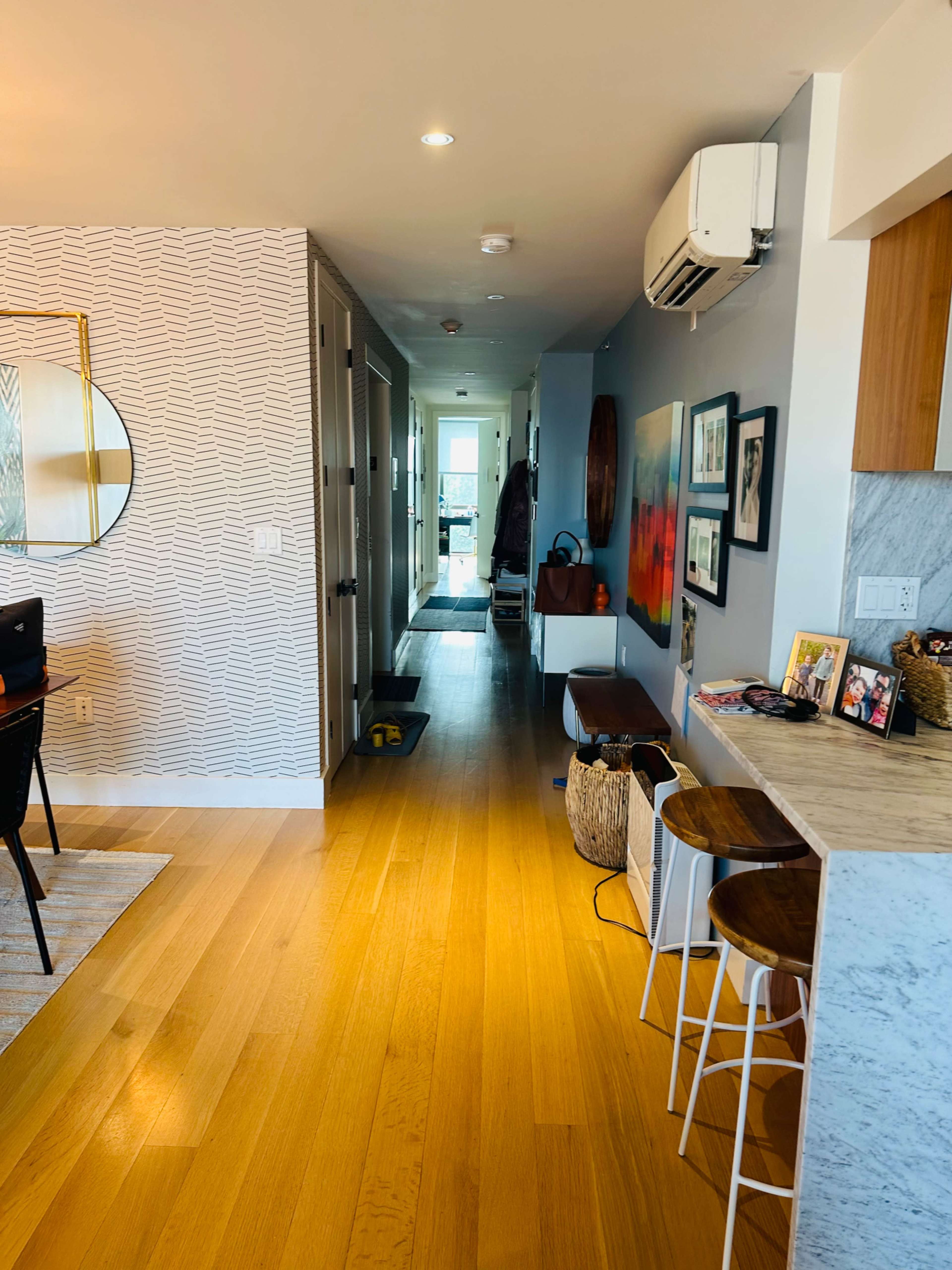 A modern hallway with light wood flooring, leading to an open space and a view of glass doors at the end.