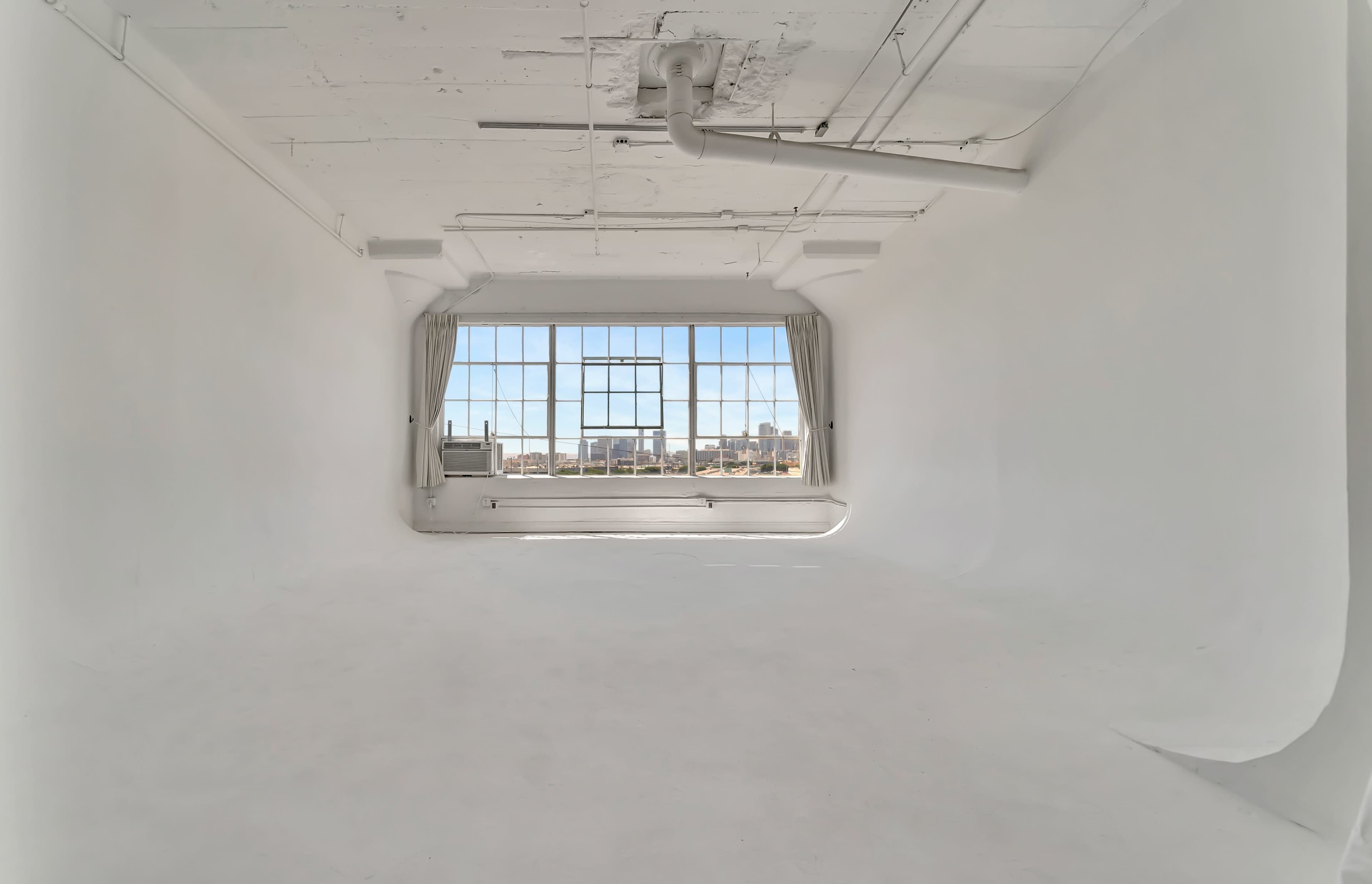 A spacious, empty studio with white walls and a large window letting in natural light.