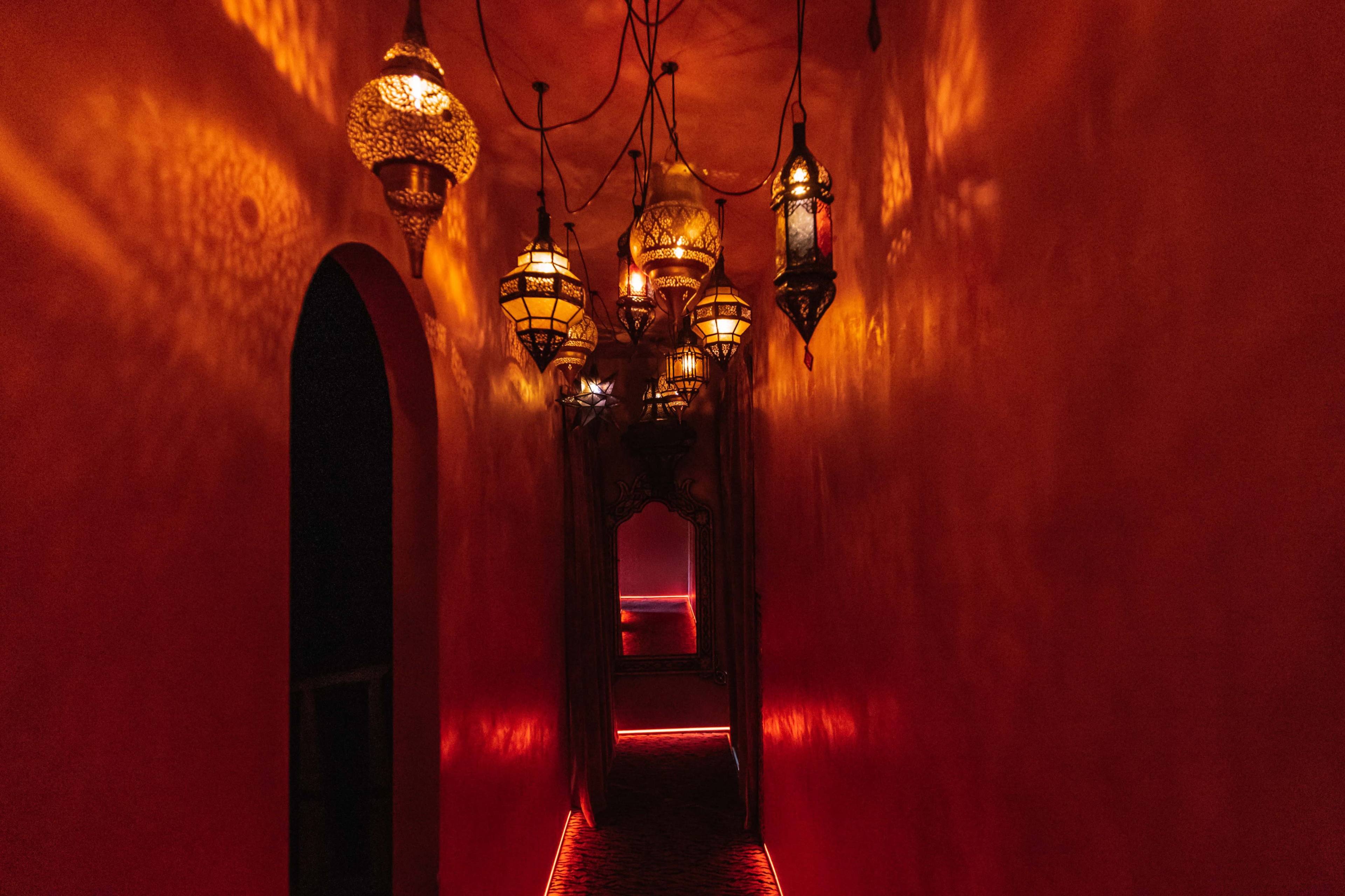 The image shows a dimly lit hallway adorned with decorative lanterns casting warm light on the orange walls.