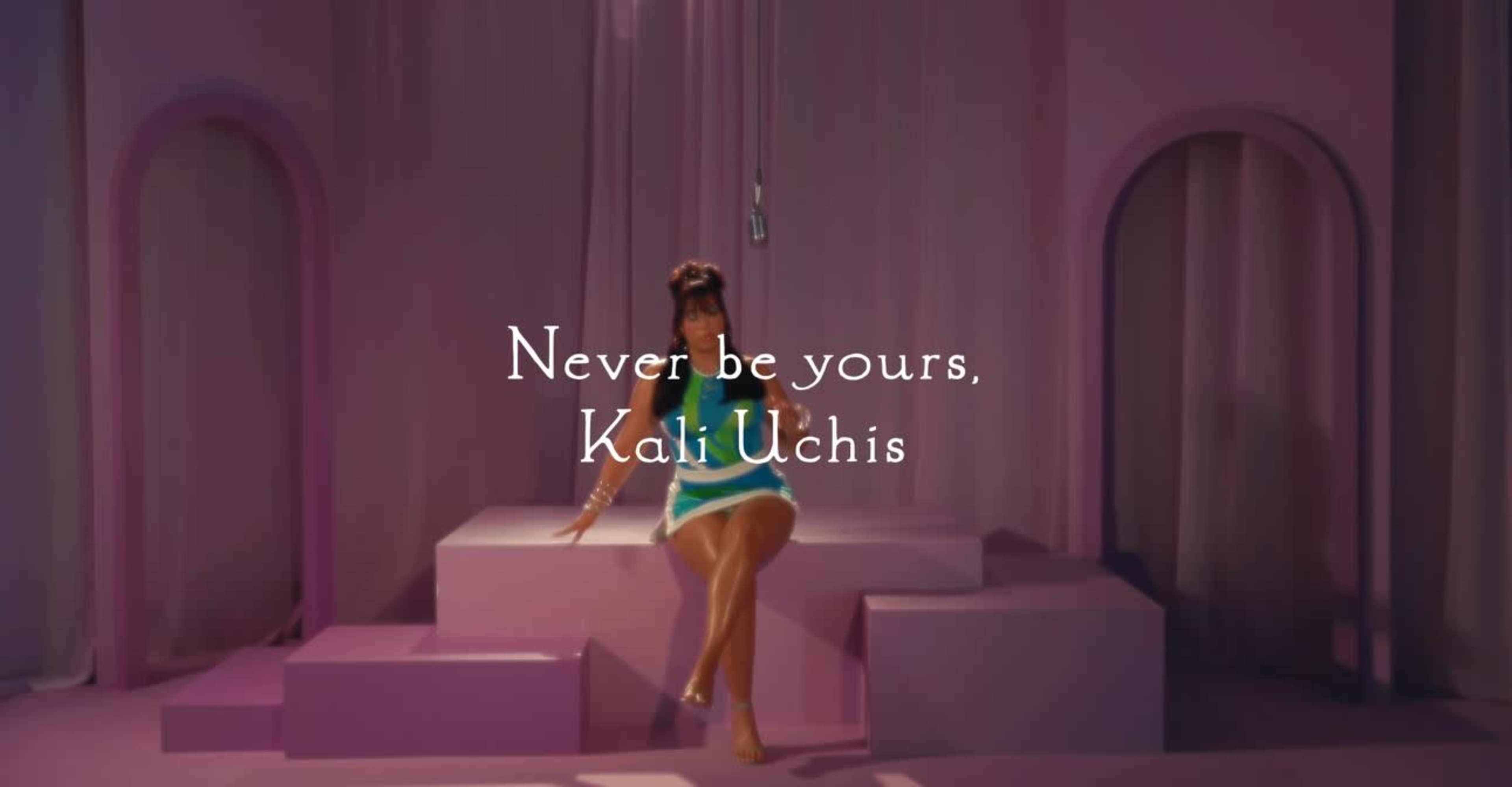 A woman sits on a pink stage with soft lighting, accompanied by the text "Never be yours, Kali Uchis."