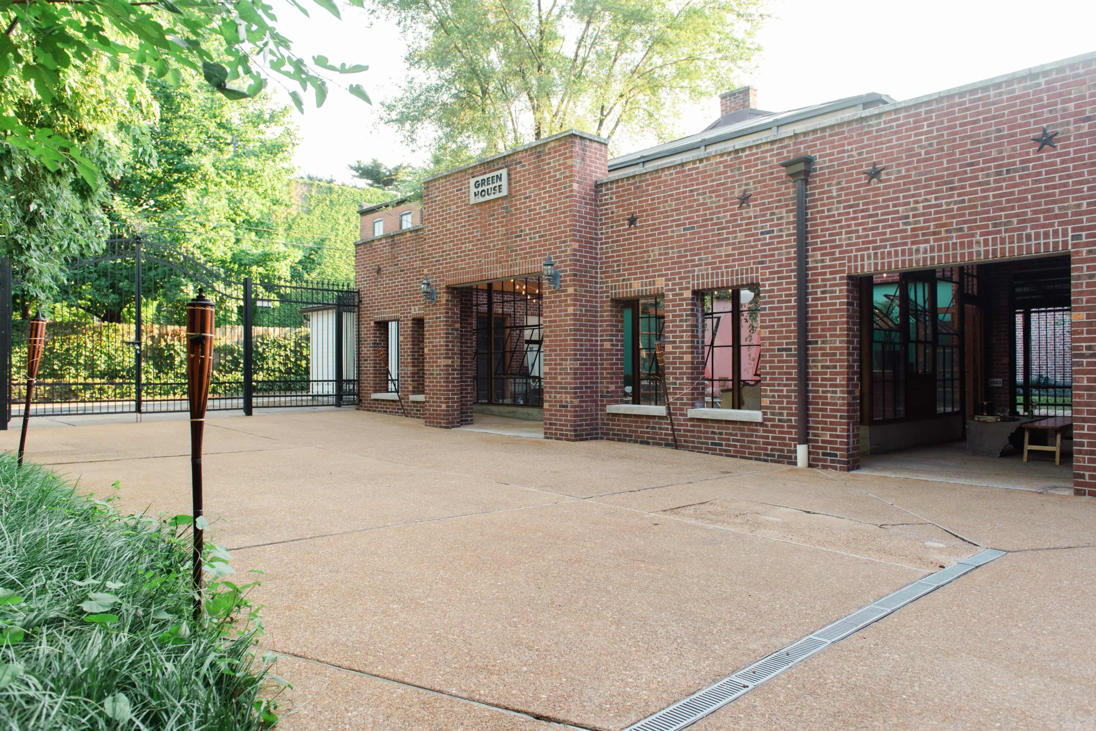The image shows a brick building with large windows and a sign that reads "Community Center," set in a landscaped area with a paved outdoor space and surrounding greenery.