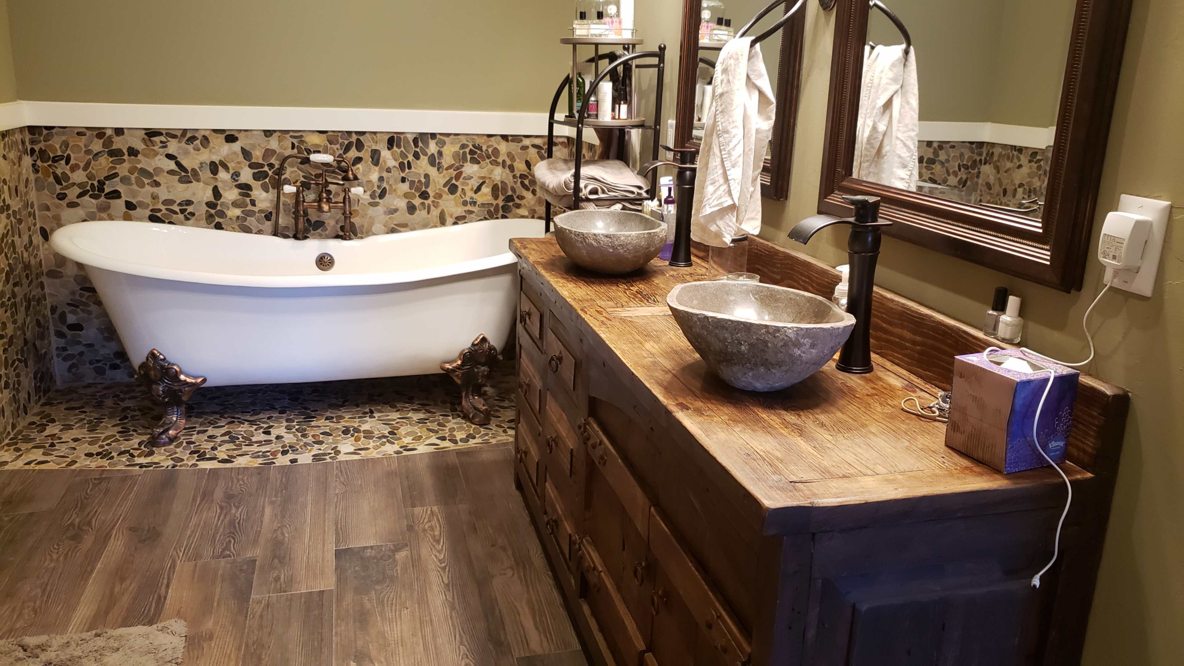 A bathroom featuring a clawfoot bathtub, a wooden vanity with stone sinks, and a pebbled wall trim.
