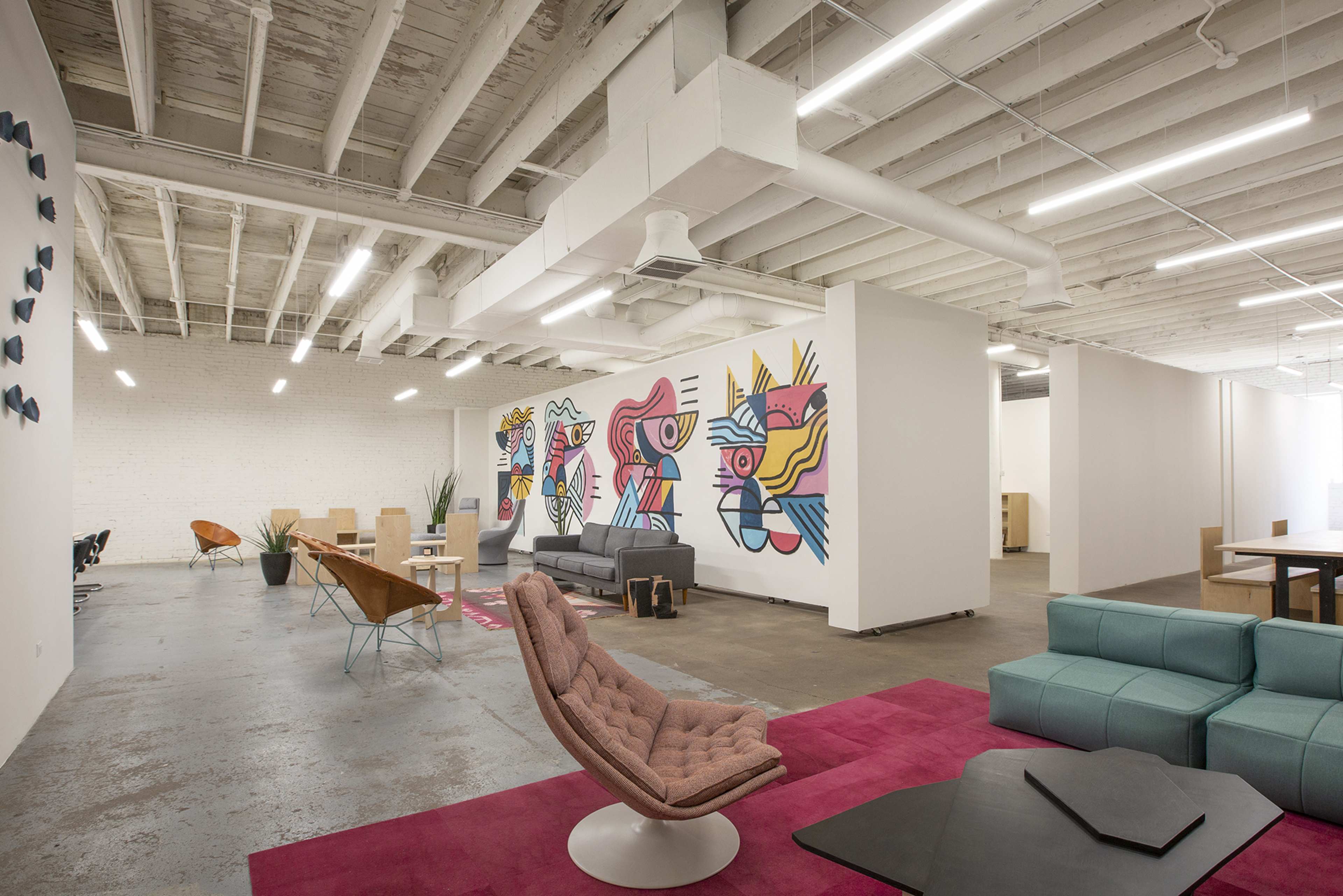 An open office space with modern furniture, colorful wall murals, and a mix of seating arrangements.